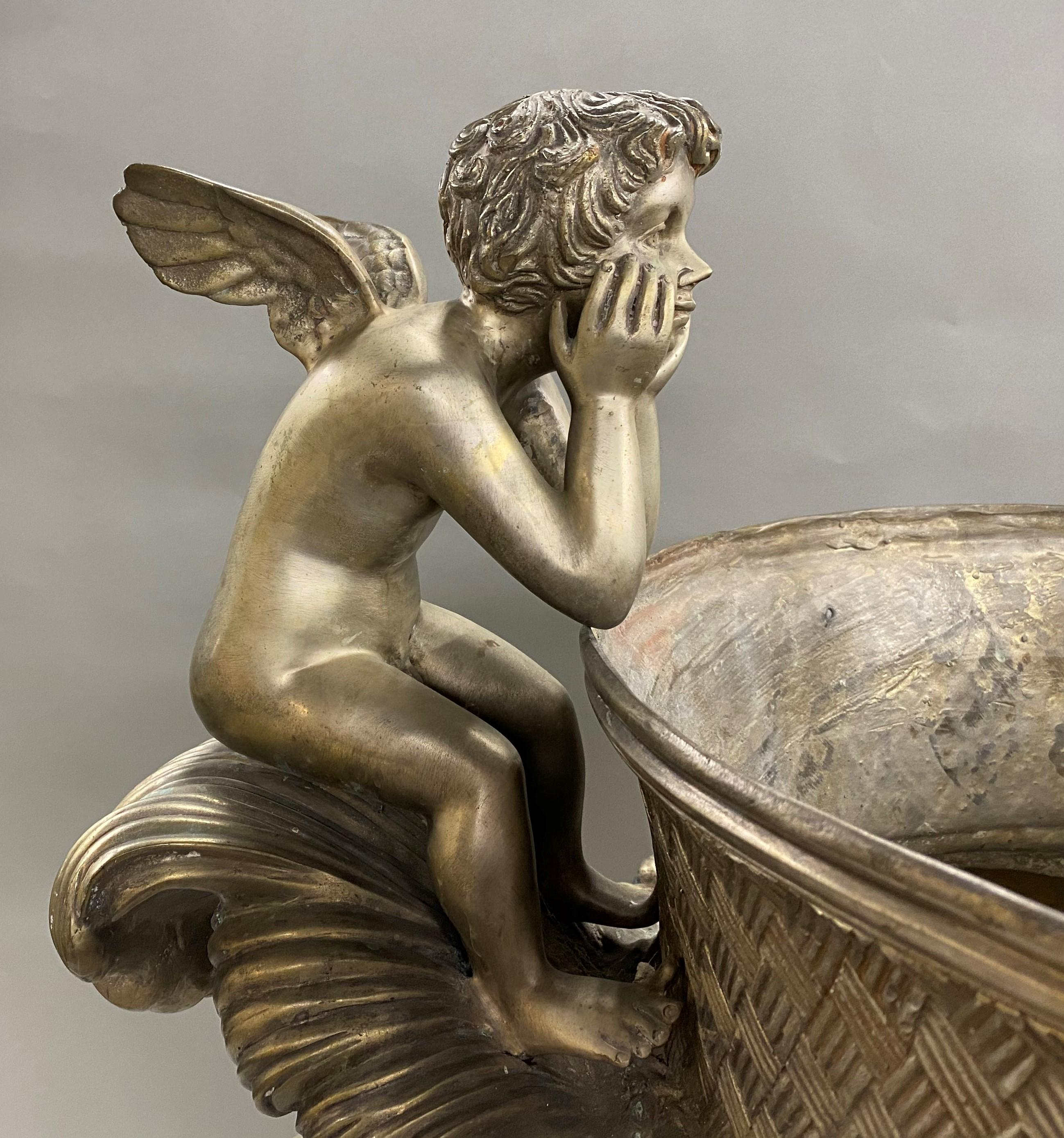 A fine silvered metal garden urn in a classic form with two winged putti seated along its woven decorated rim above lion head handles, the sides adorned with floral garland, and a foliate decorated round base. The urn dates to the 20th century and