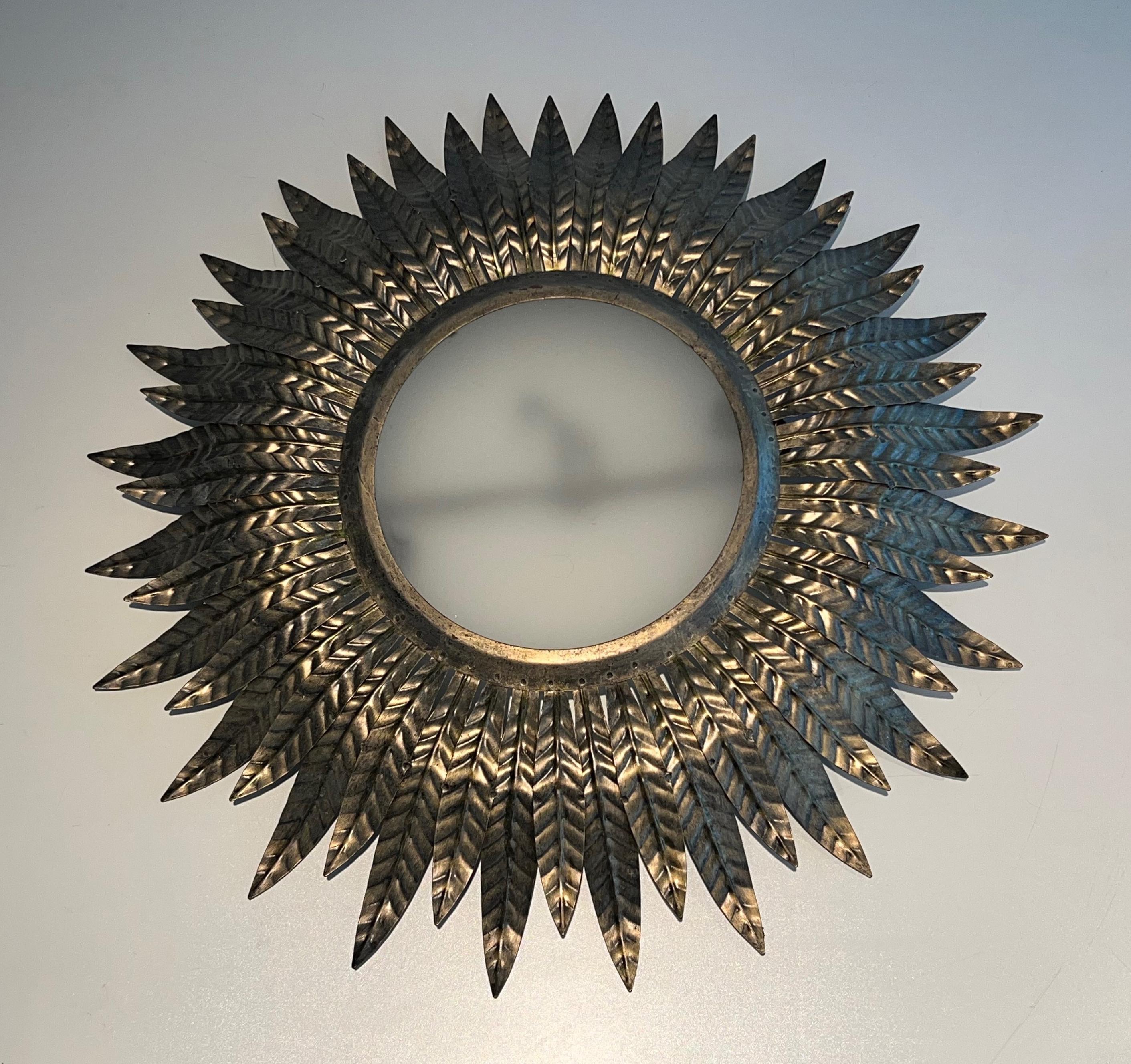 Ce joli luminaire ou applique décorative en forme de soleil est fait de métal argenté avec un rond de verre opaque en son centre. Il s'agit d'un ouvrage français. Circa 1970