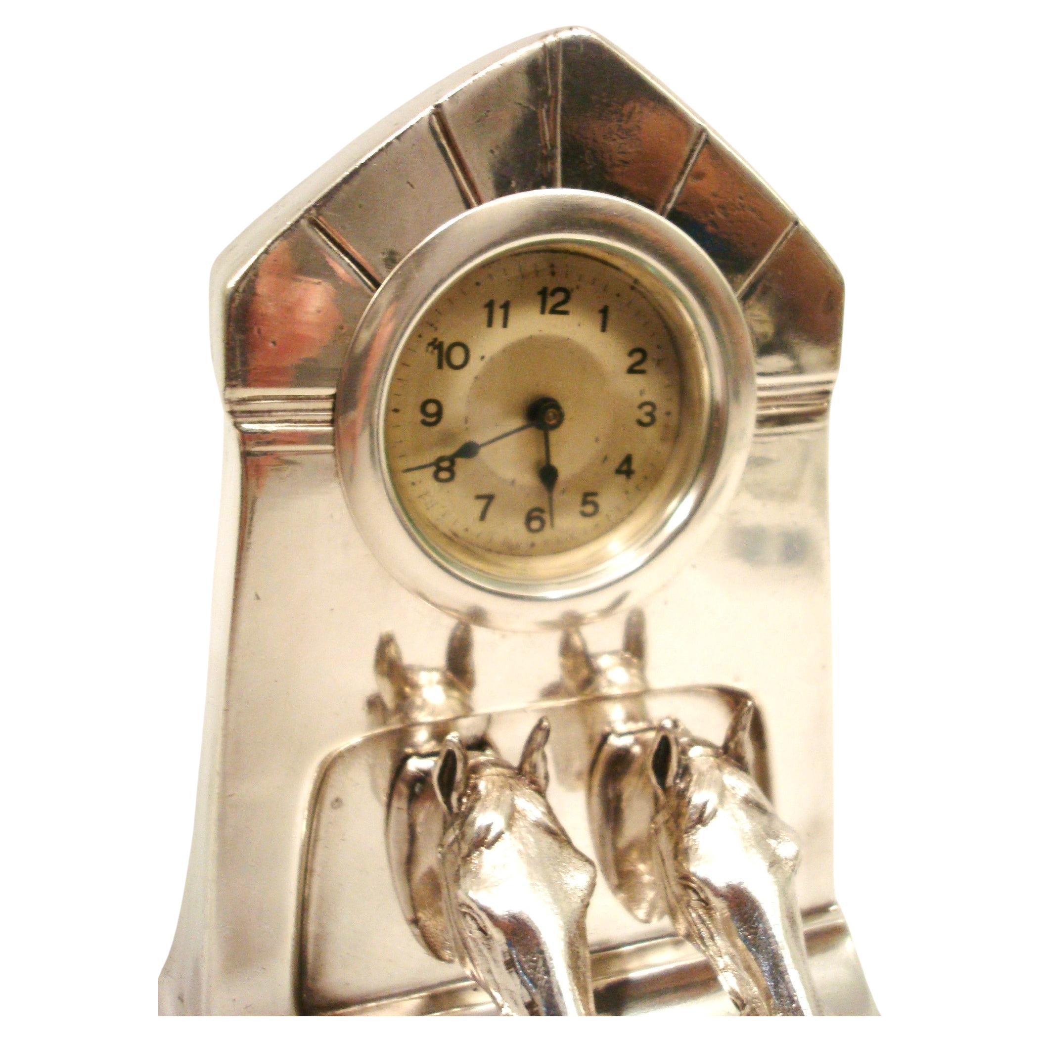 
Horloge de table argentée. L'horloge a un sommet arrondi et une base rectangulaire. Le cadran de l'horloge est circulaire, avec des chiffres et des aiguilles noirs, et il est encastré dans la partie supérieure de la structure. Sous le cadran de