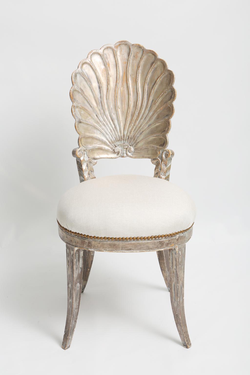 Single grotto style side chair, having a silver gilt finish showing natural wear, its back hand carved as a scallop shell, to a round, stuff-over seat of linen with nailheads, raised on sabre legs.

Stock ID: D2090.