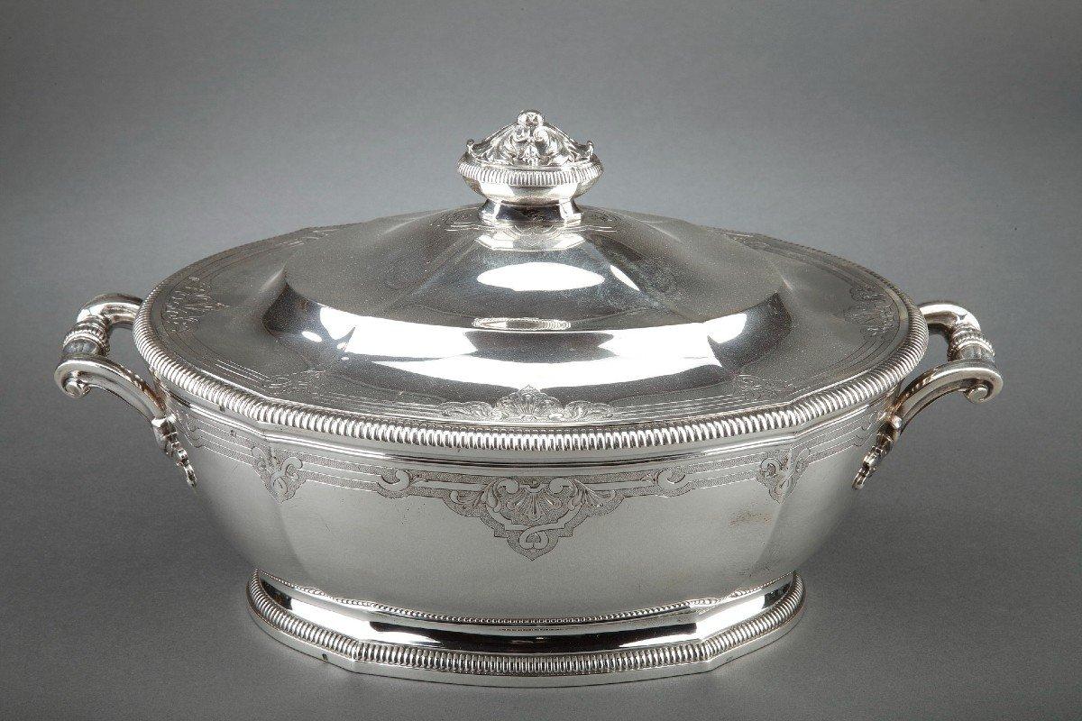 Oval covered tureen in solid silver, it rests on an oval bate with pinched ribs and surrounded by a gadroon. The belly and the lid are engraved with a Berain decoration on a matte background. the cove lid is surmounted by a grip formed by two