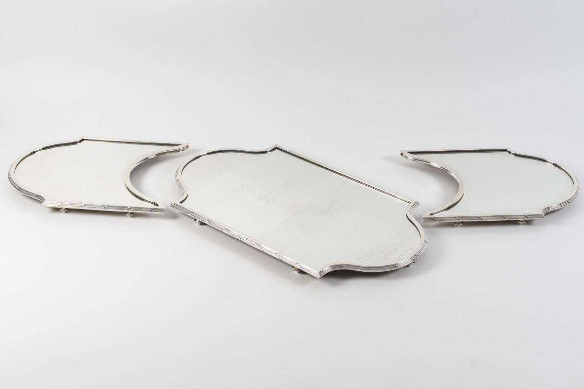 An important three-part Louis XVI-style centerpiece with a mirrored back, on a wooden parquet floor, set with a large solid silver ingot mold with crossed threads and ribbons, mounted on spinning top feet.

Dimensions: Total length 139 cm - Center: