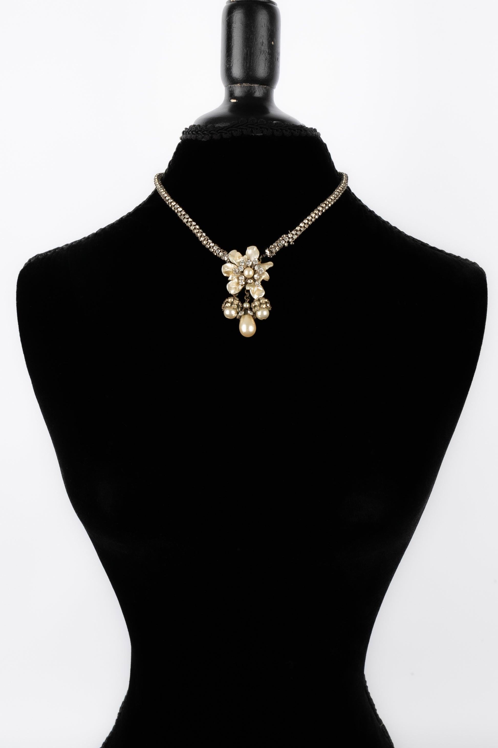 Unknwon - Silvery metal short necklace with rhinestones and a pearly flower pendant. Not signed antique jewelry. To be mentioned, the chain is a bit damaged.

Additional information: 
Condition: Good condition
Dimensions: Length: 41 cm
 
Seller