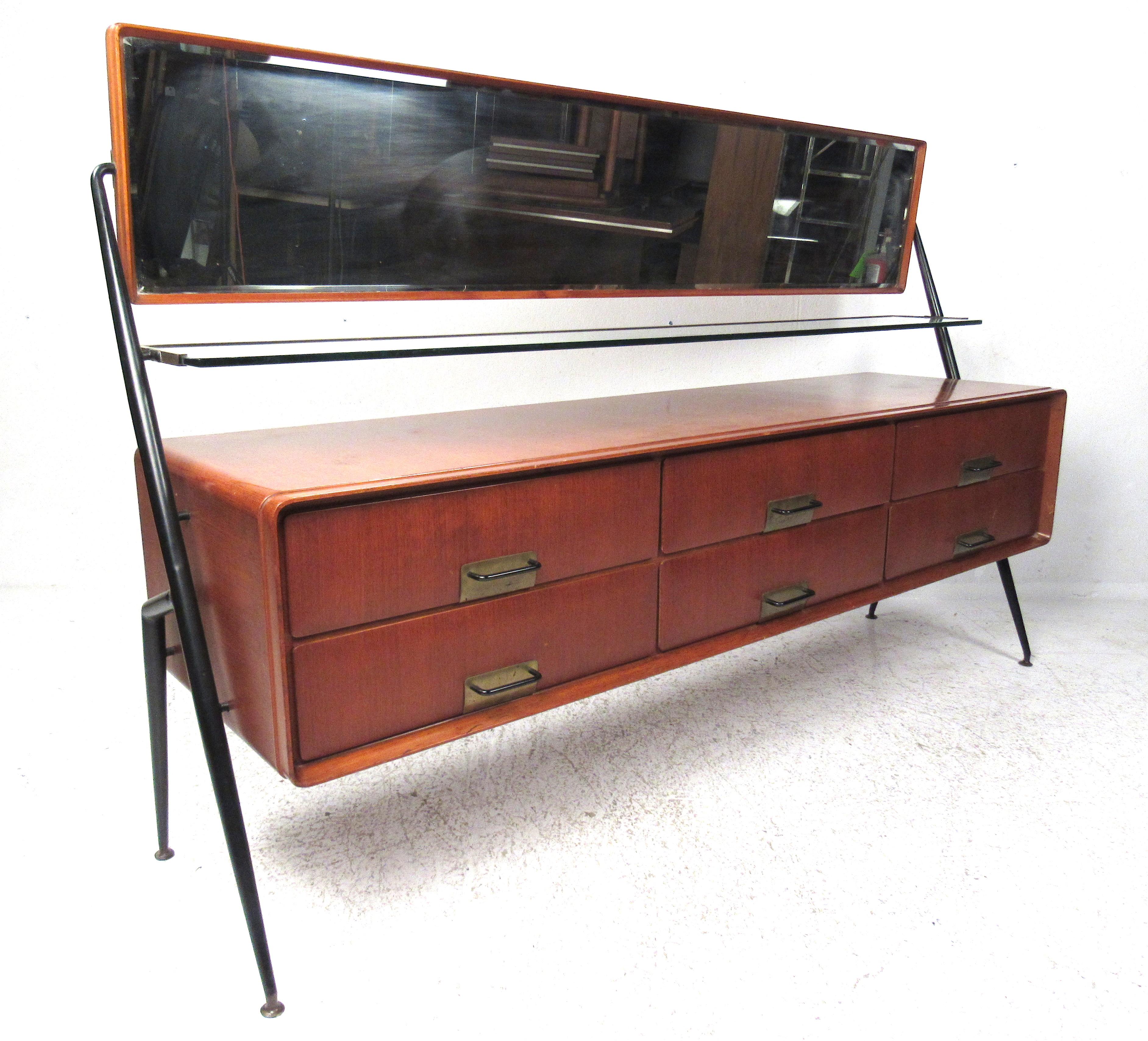 Silvio Cavatorta mahogany cabinet with six drawers, horizontal tilting mirror, and glass shelf with brass trim.
All supported by angular steel legs with brass feet, circa 1960s.