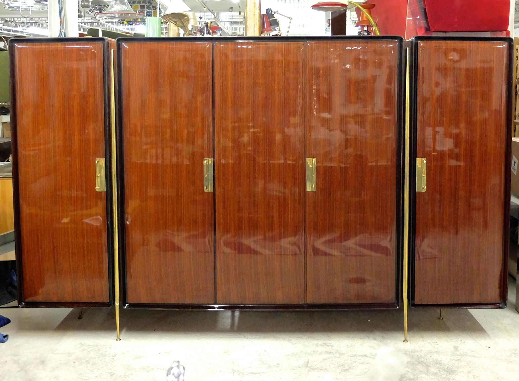 A five-door Italian mahogany and brass armoire by Silvio Cavatorta for SC Roma, circa 1950. High gloss polished clear coat finished exterior and black edge trim. Fully fitted gloss clear coat satinwood interior. Comprised of three case units which