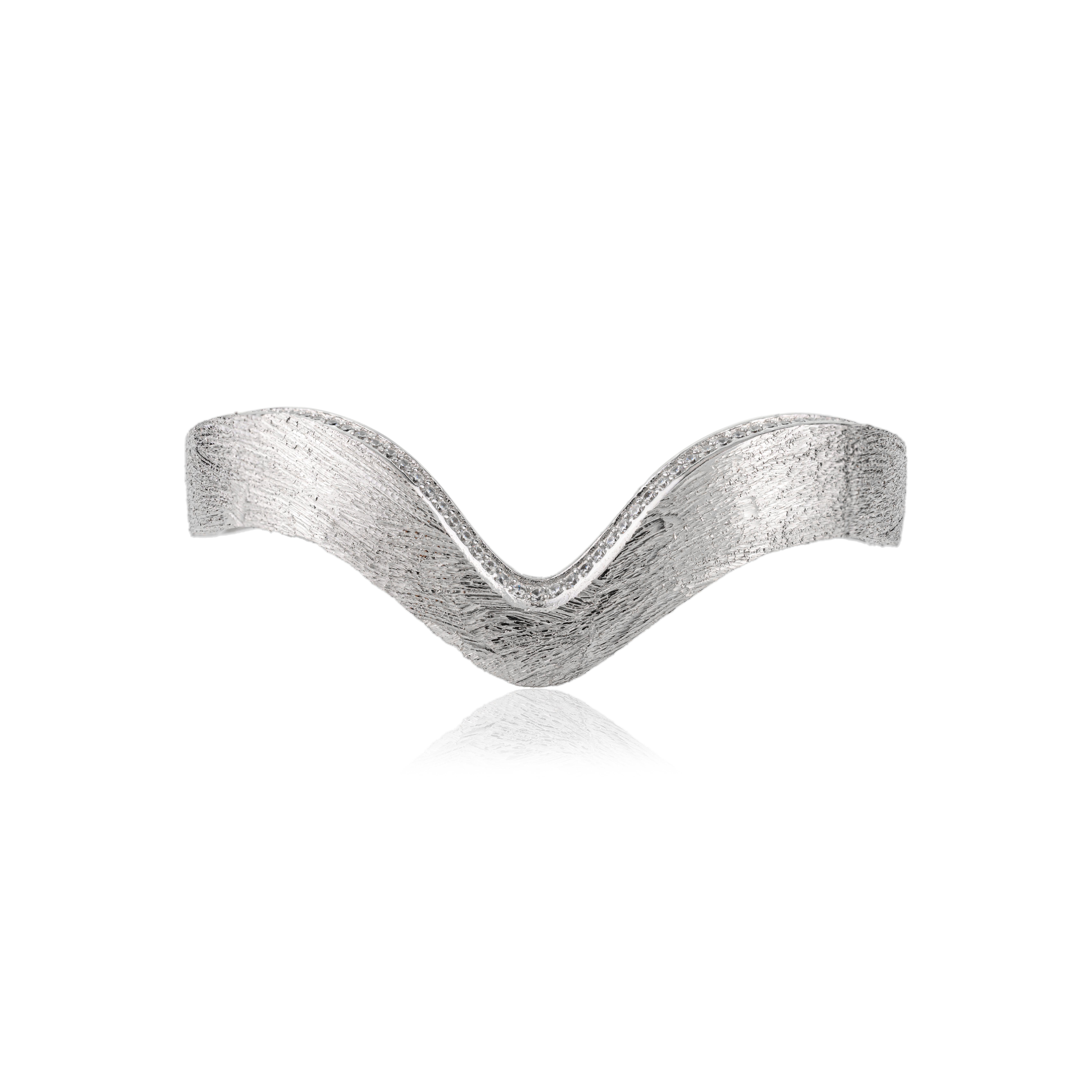 Ce bracelet manchette contemporain en argent massif 925 présente une silhouette élégante et ondulée avec une finition de texture brossée. Délicatement rehaussé de pierres rondes en zircon cubique de 1 mm, il offre une subtile touche d'éclat. Pesant