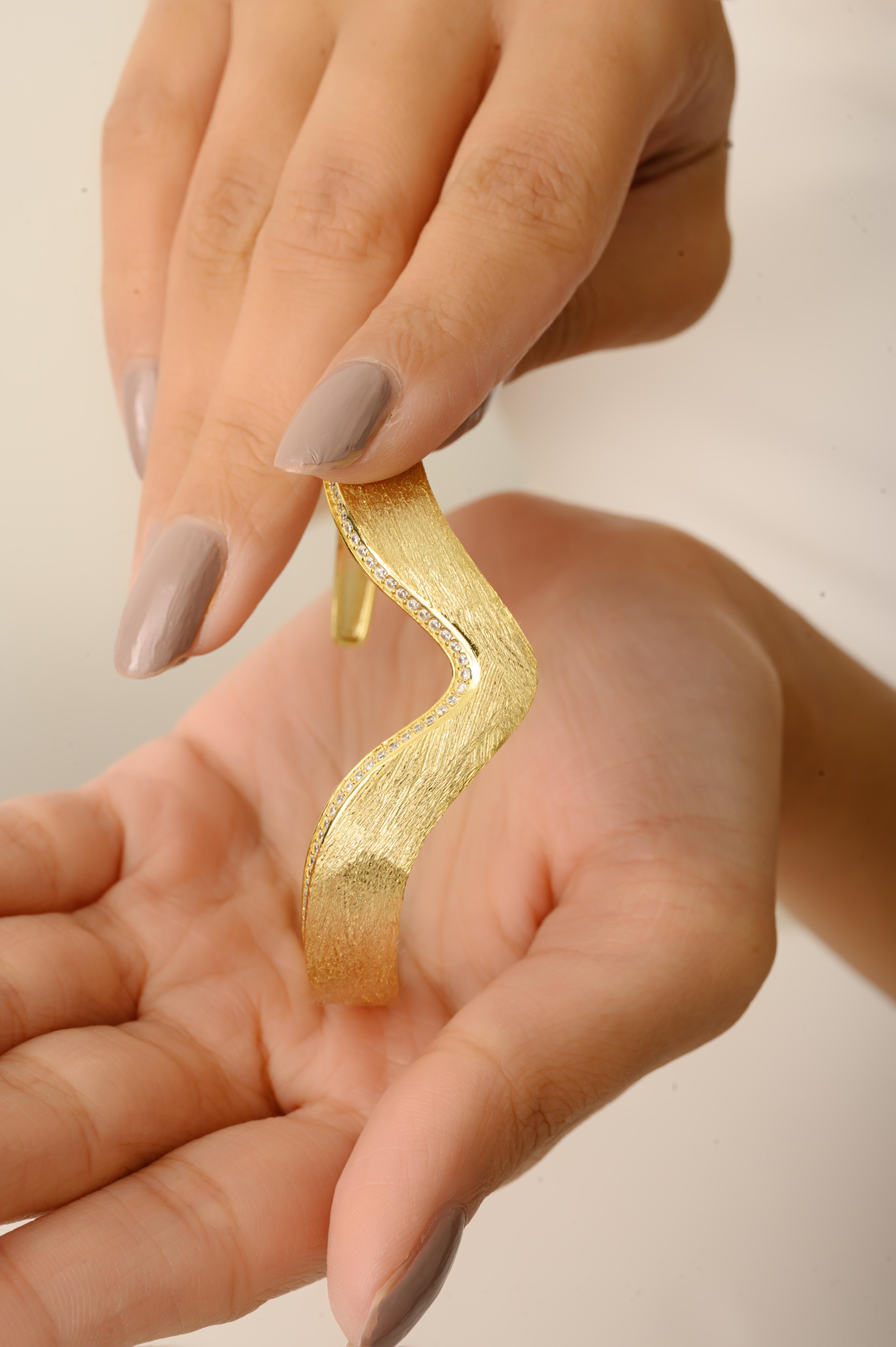 Questo bracciale bangle in argento sterling 925 realizzato a mano presenta un elegante design ispirato alle onde, rifinito con una lussuosa texture dorata opaca. Ornato da delicate pietre di zirconia cubica da 1 mm che brillano sottilmente lungo la