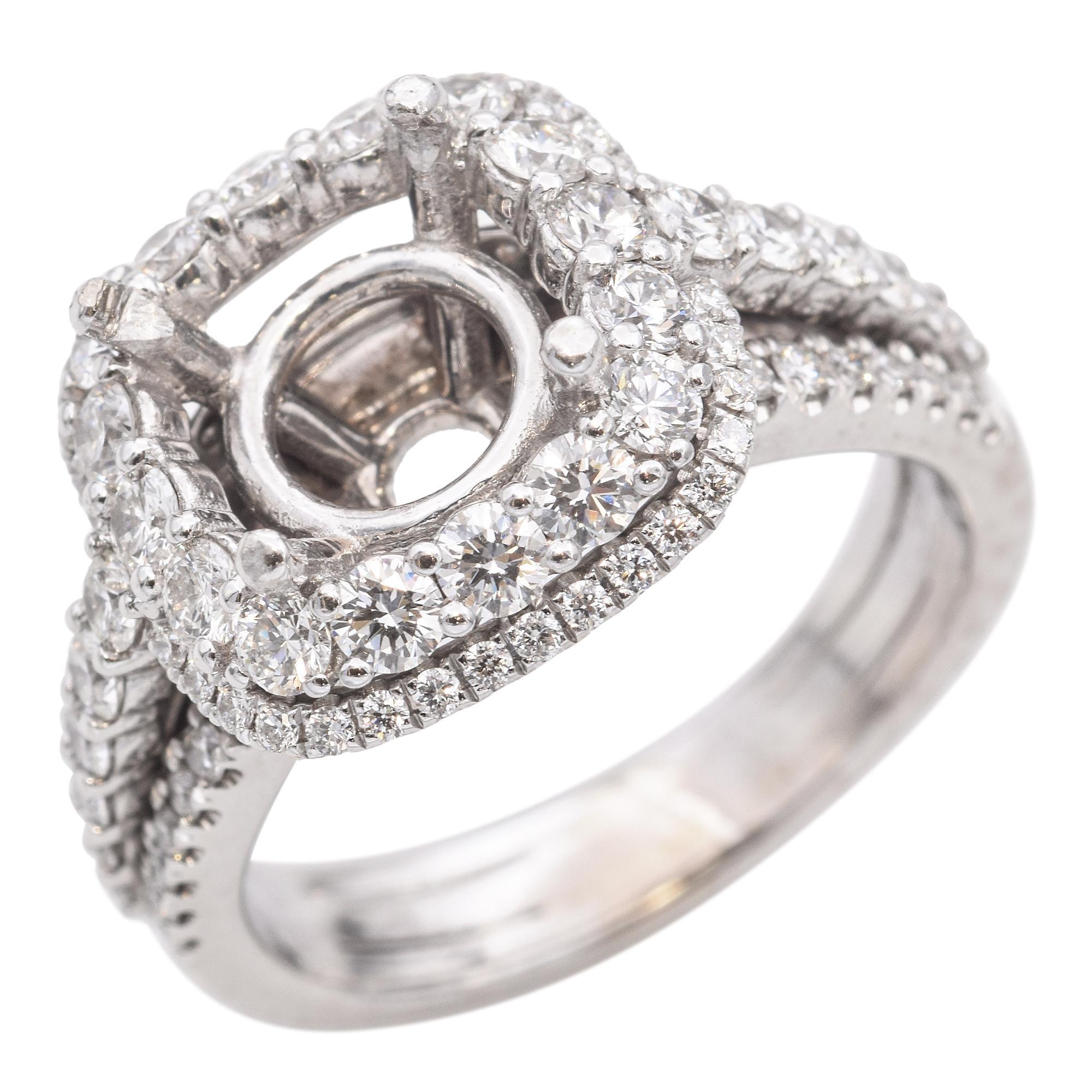 Cette bague exquise présente un double halo incrusté de diamants ronds brillants. La monture est conçue pour accueillir une pierre centrale, entourée d'un halo de diamants plus petits en forme de coussin. La bande est ornée de diamants