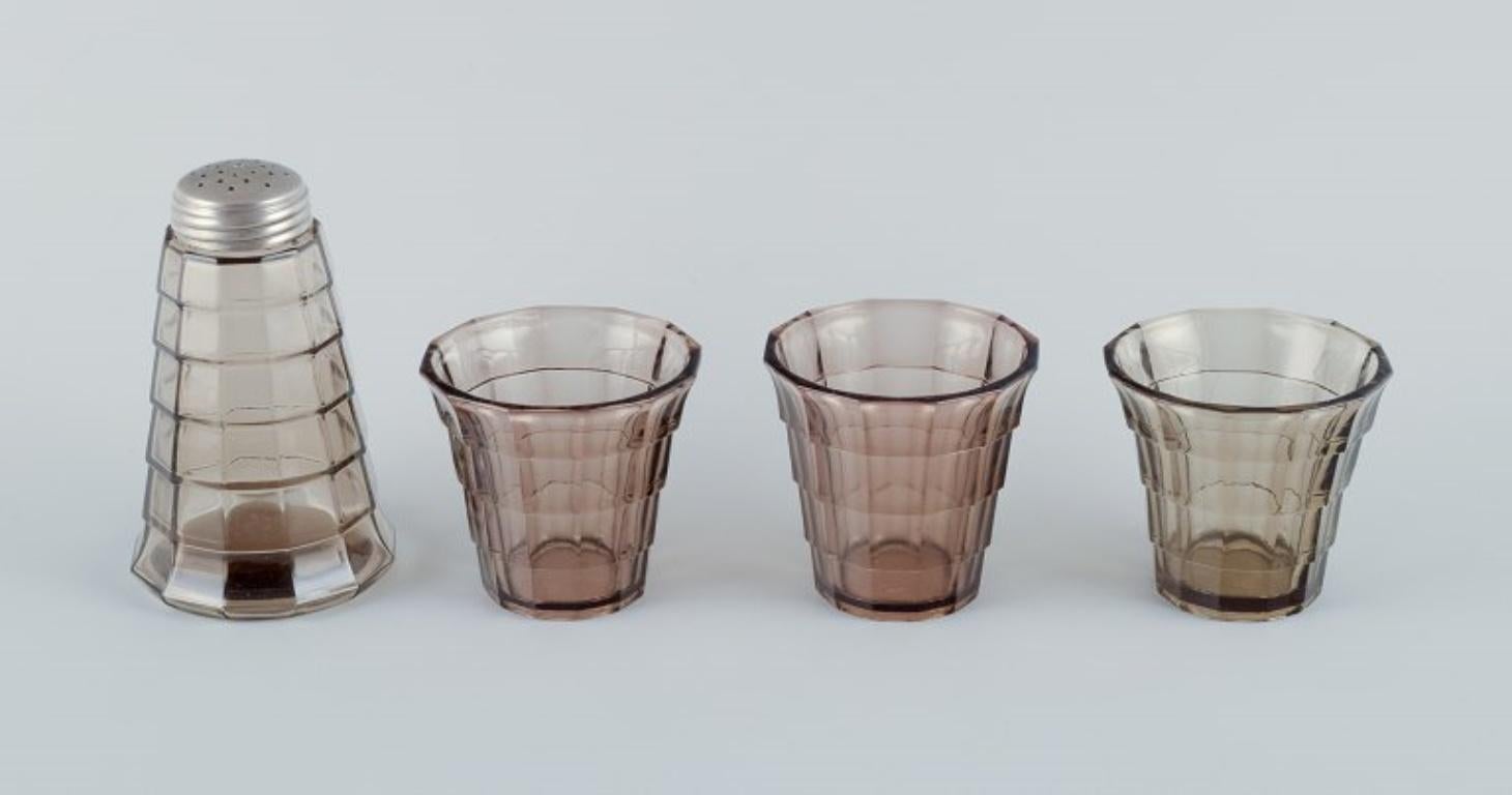 Simon Gate (1883-1945) for Orrefors/Sandvik, Sweden.
A set of three drinking glasses and a sugar shaker in Art Deco style, in smoked-coloured pressed glass.
Model G756.
Approximately from 1940.
In perfect condition.
Height of drinking glasses: 6.7