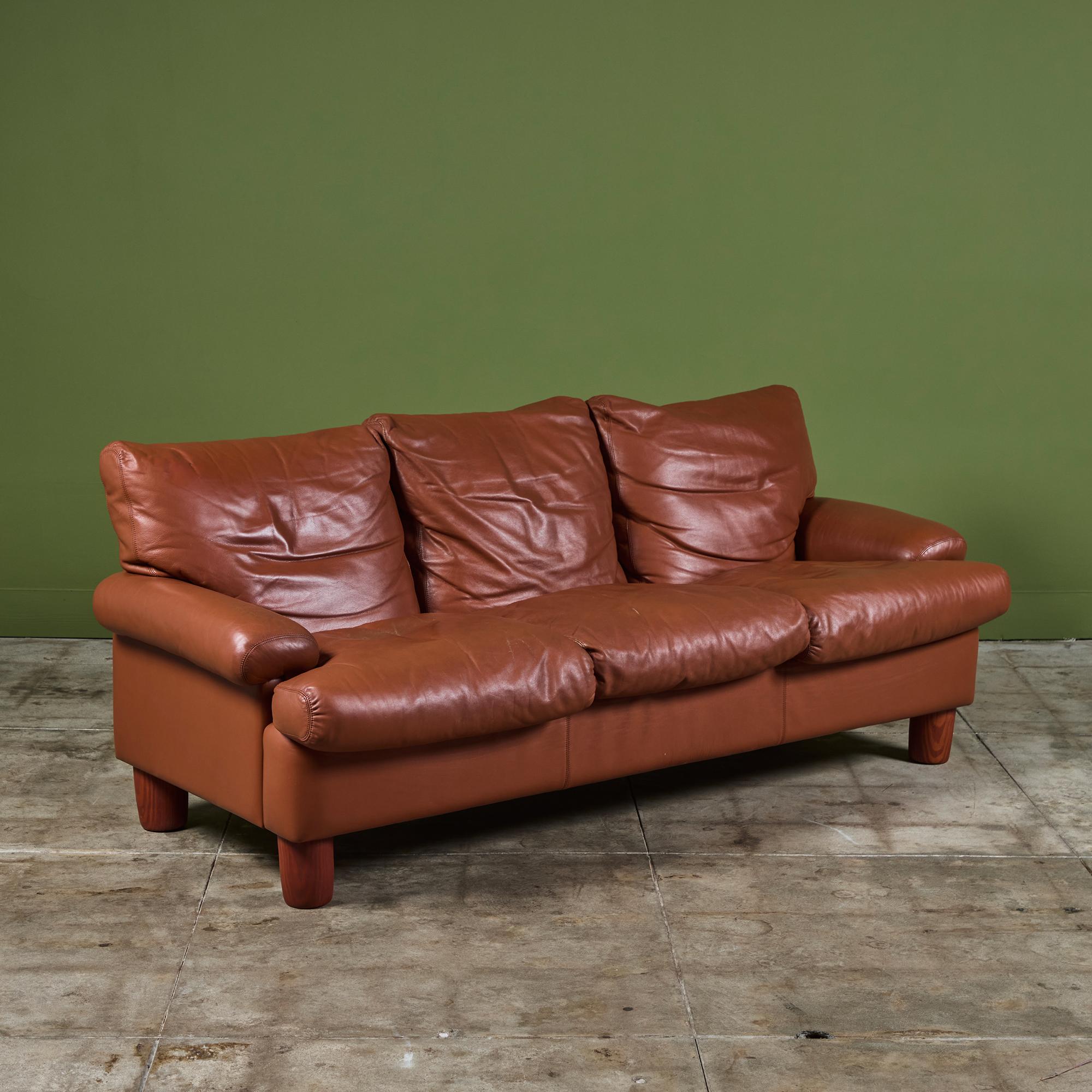 Leather sofa by Ferdinando Buzzi for Brunati c.1970's, Italy. The three seater sofa features wide armrests and three down-filled backrest and seat cushions for a comfortable seat. The sofa rests on four wood peg legs.

Dimensions
81.25” width x 37”