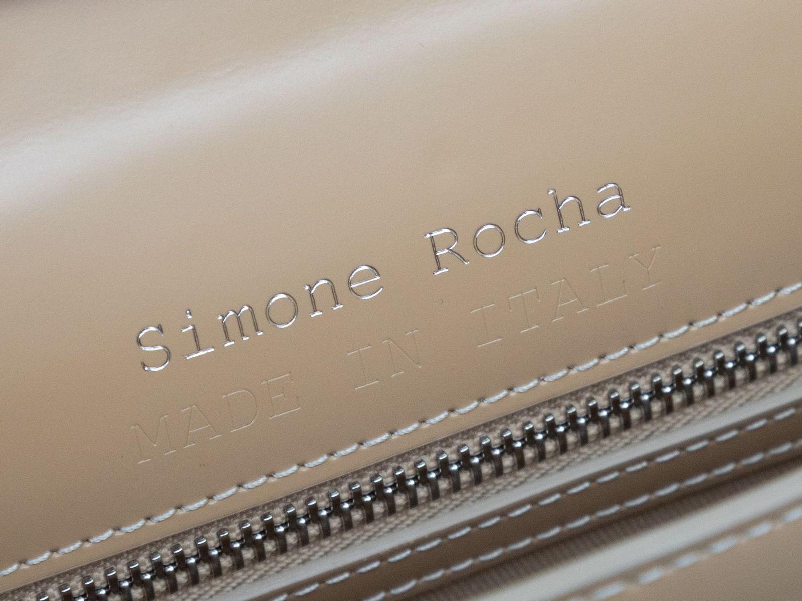 Product Details: Beige Simone Rocha Leather Bean-Shaped Handbag. This shoulder bag features a smooth leather body, a single flat top handle, and a front magnetic flap closure. 11