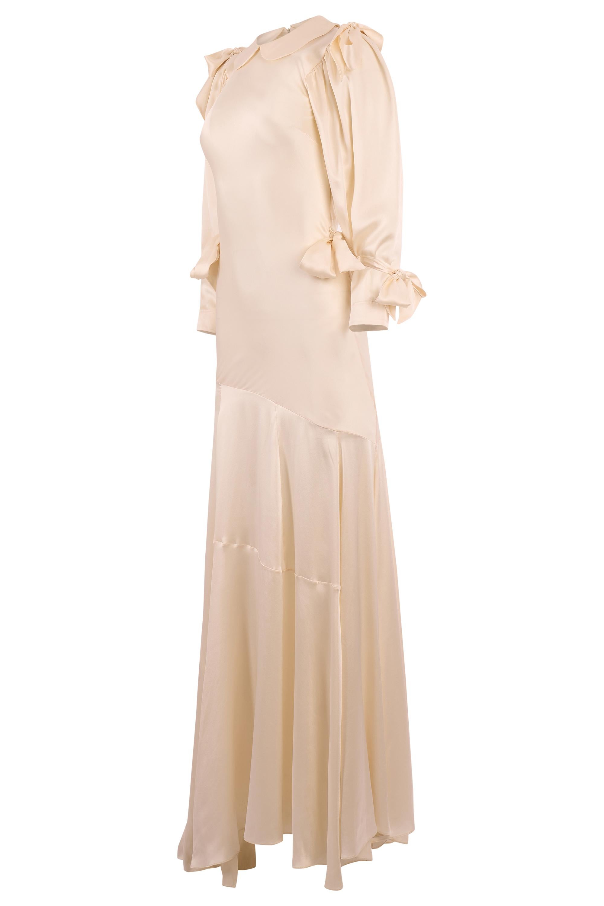 Simone Rochas printemps été 2024 Robe longue en soie blanc crème avec nœud. La robe présente un drapé dramatique en forme de nœud aux épaules et des accents de nœud supplémentaires aux poignets des manches et à la taille, un col plat arrondi et se