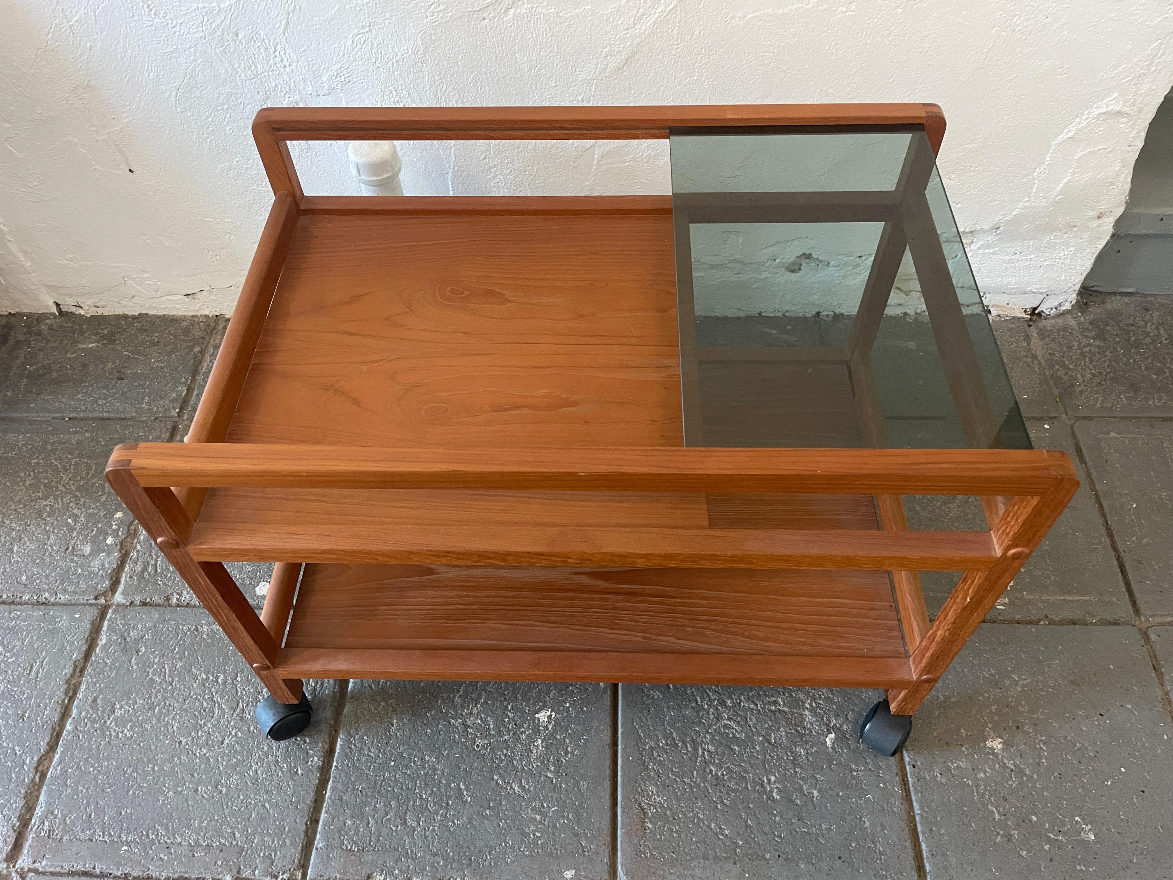 Simple mid-century Danish modern teak bar cart server with sliding smoked glass top shelf on casters. Solid teak wood construction. Original vintage condition clean all around. Located in Brooklyn NYC. 

Measures 27” W x 18” D x 20” H.