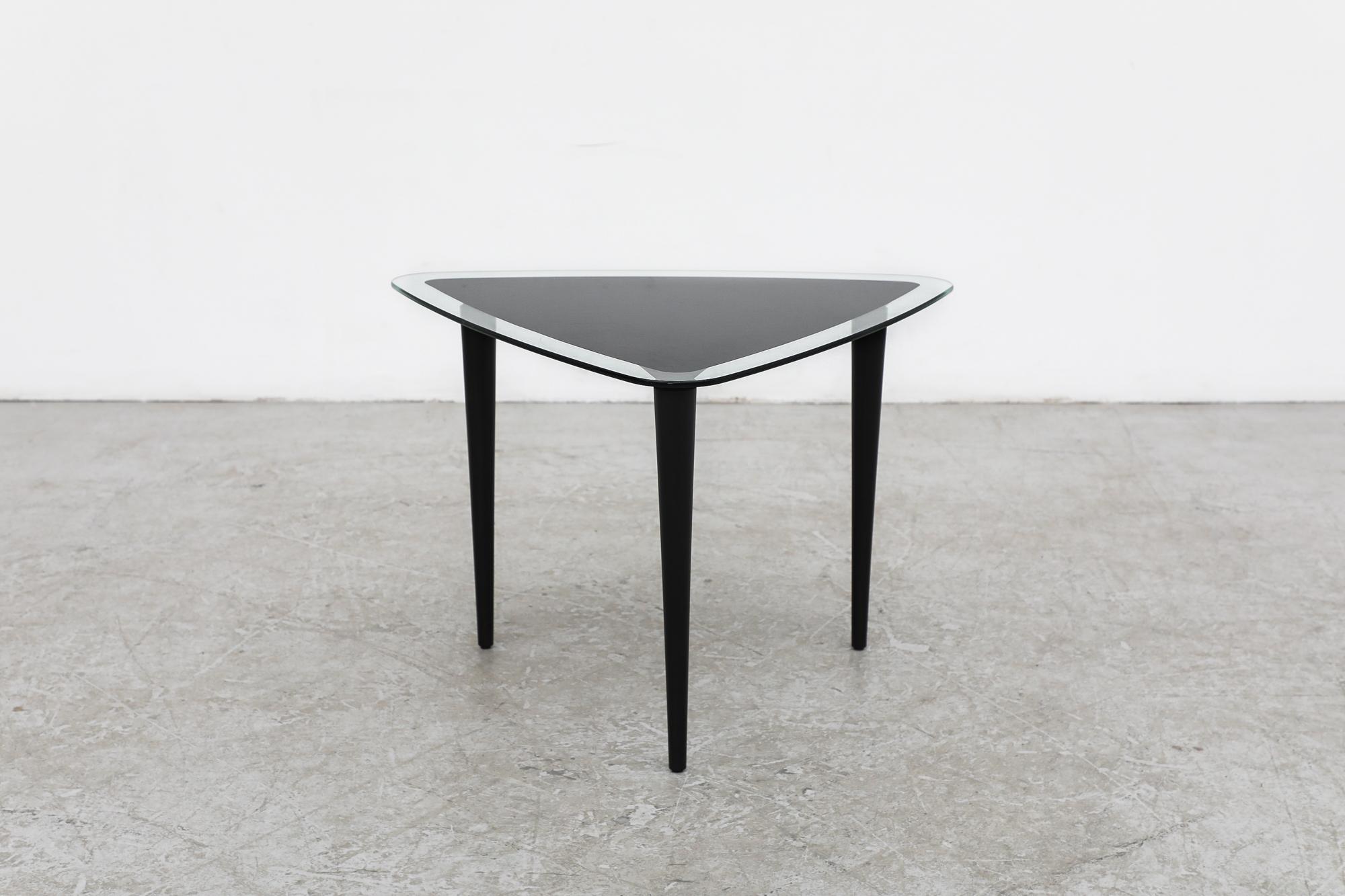Mid-Century Modernist glass triangular side table with tapered legs. The top has a black printed triangle in the center of glass with clear glass boarder and three black tapered wood legs. In original condition with visible wear, including