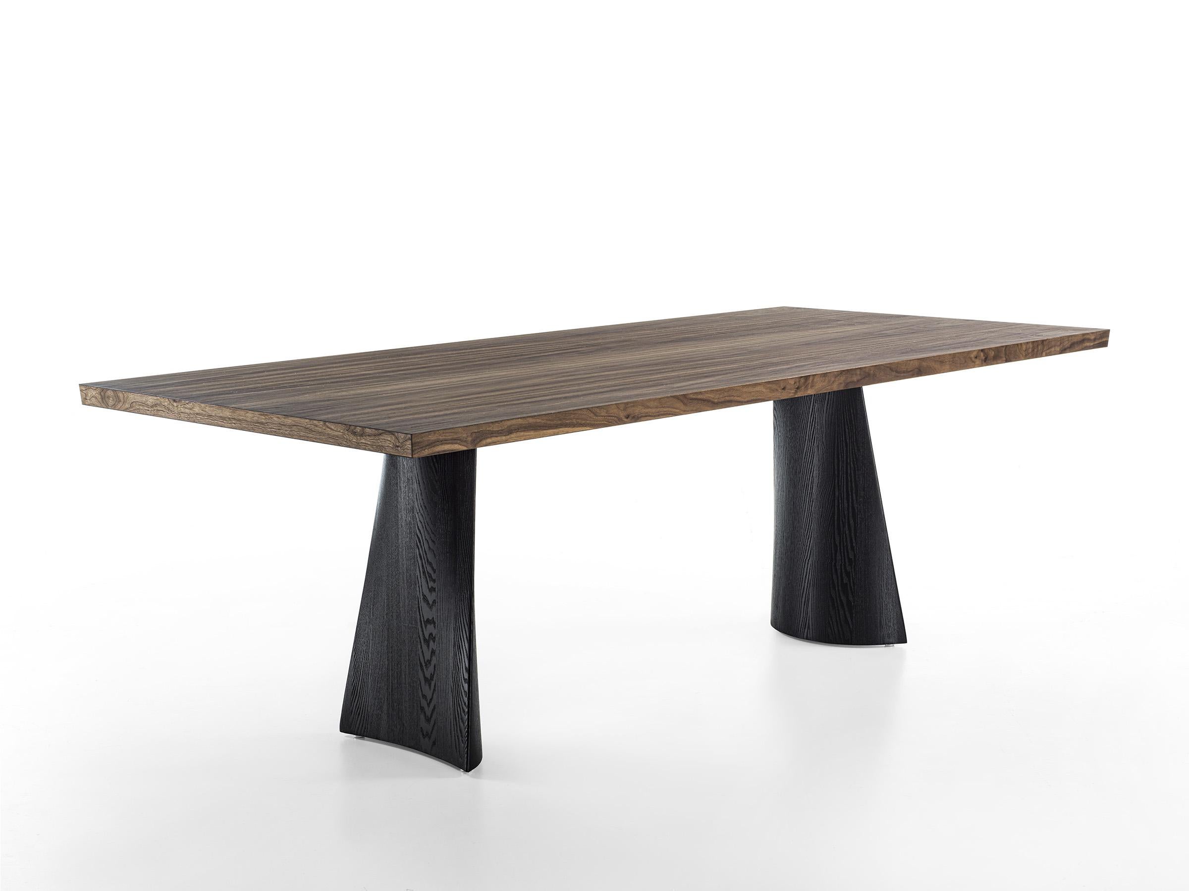 Table made with blockboard veneered top and bevelled edges. It is characterized by two solid wood legs in pigmented finish. The shape of the base comes from a play of curved and straight lines, that give it lightness. Legs in solid ash wood,