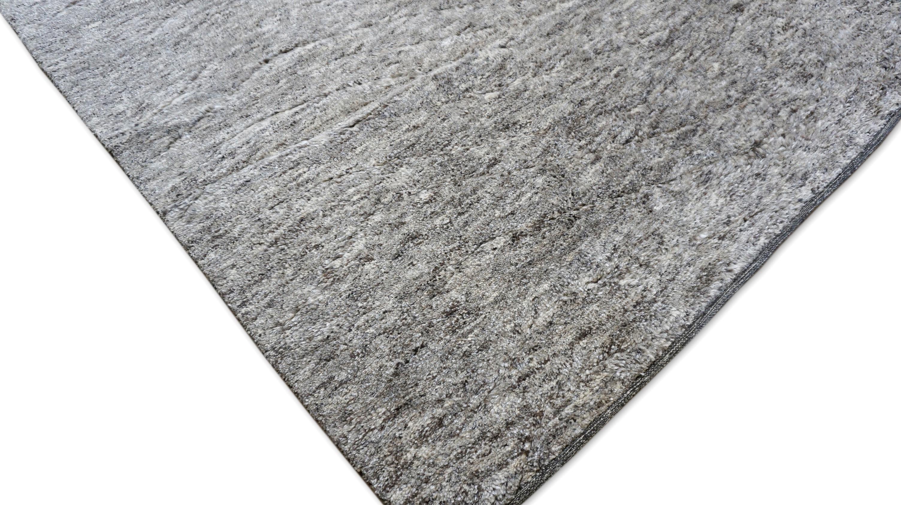Exemplaire de l'art du luxe discret, ce tapis en laine noué à la main présente une surface moelleuse et profondément texturée, aussi accueillante que sophistiquée. Les tons subtilement panachés de marron naturel et de gris du tapis sont mélangés de