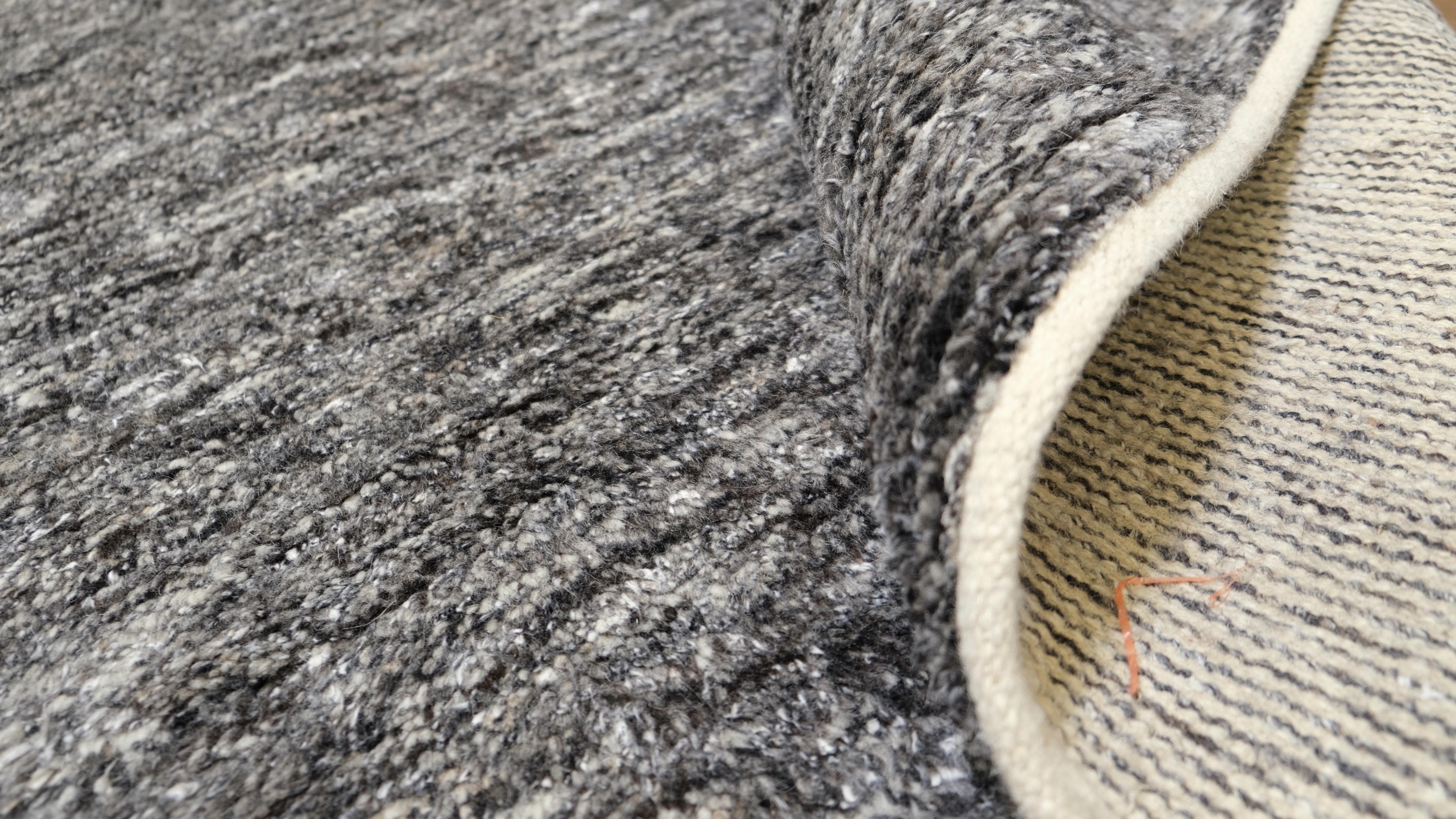Dieser handgeknüpfte Wollteppich ist ein zeitloses Stück, das moderne Eleganz mit natürlichen Texturen verbindet. Die monochrome anthrazitfarbene Palette bietet einen vielseitigen und raffinierten Look und ist damit die ideale Grundlage für