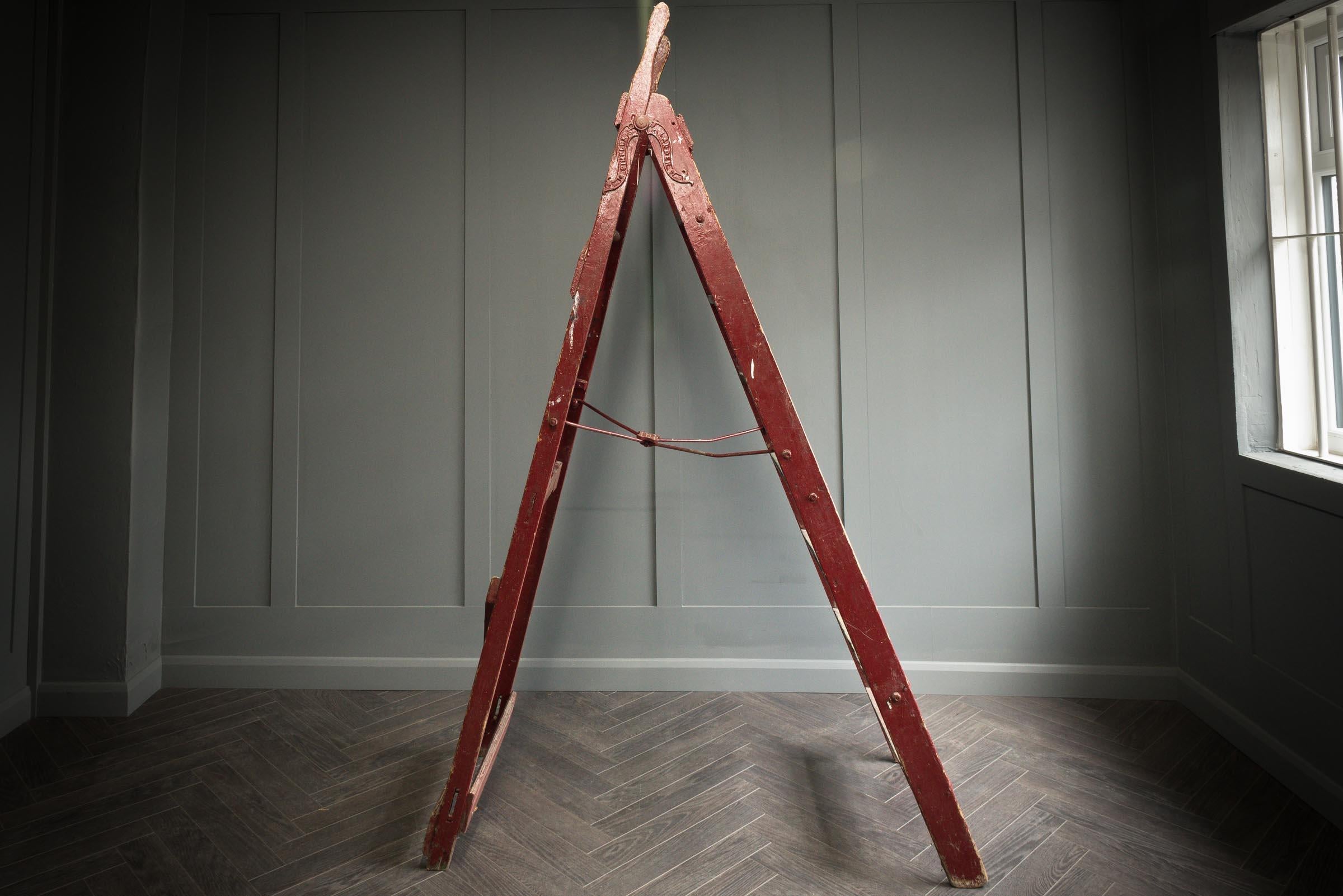 An original large simplex wooden step ladder in a bold red wash, consists of seven steps. The ladder closes by two metal hinges either side of the ladder. The ladder has original paint marks consistent with age and use. This ladder is typical of the