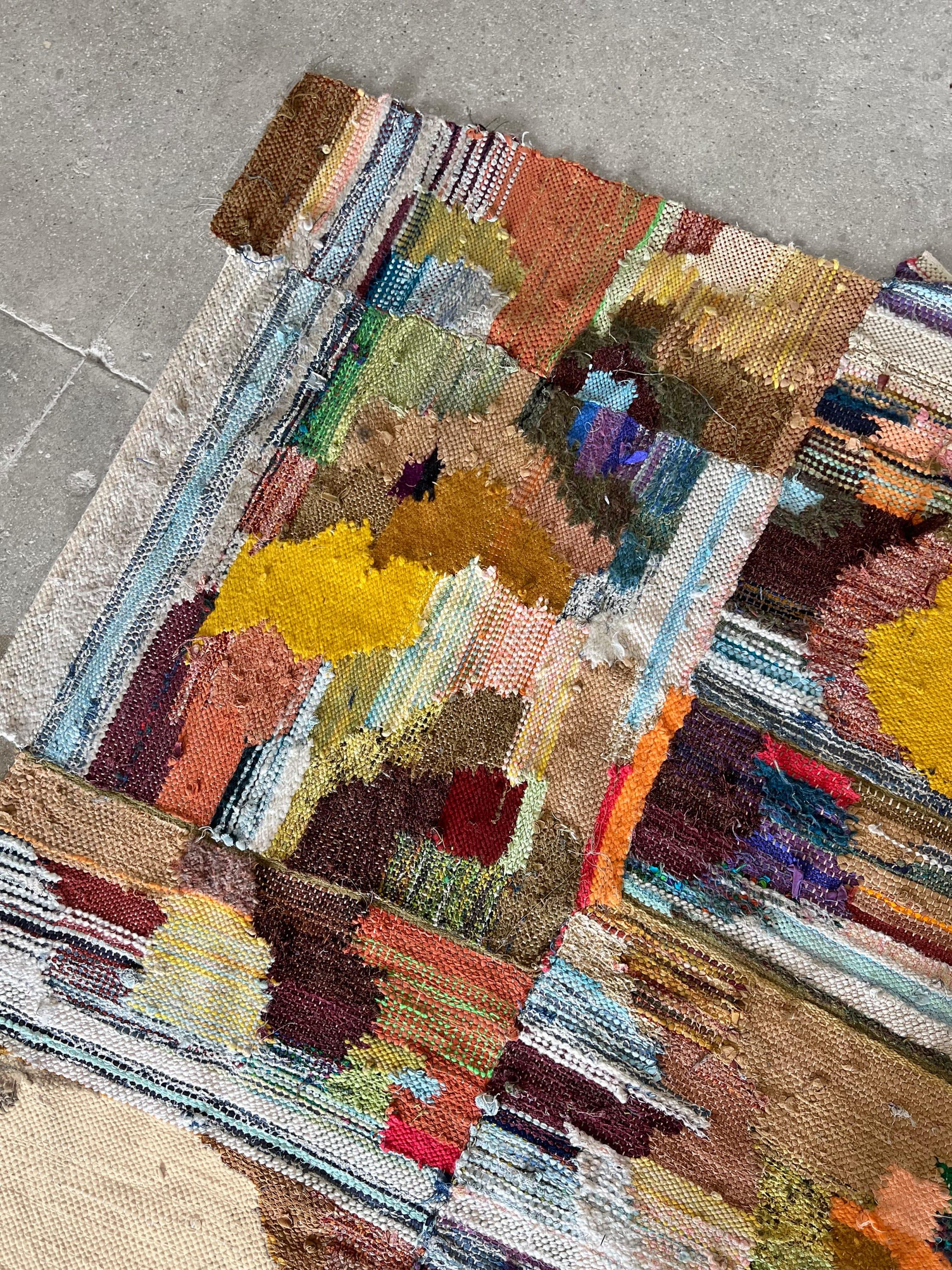 Large hand-woven tapestry made from reclaimed and new materials in the colors of yellow, orange, green, brown, and blue.  Each thread tells a story, woven together in a vibrant symphony of multicolored hues that breathe new life into forgotten