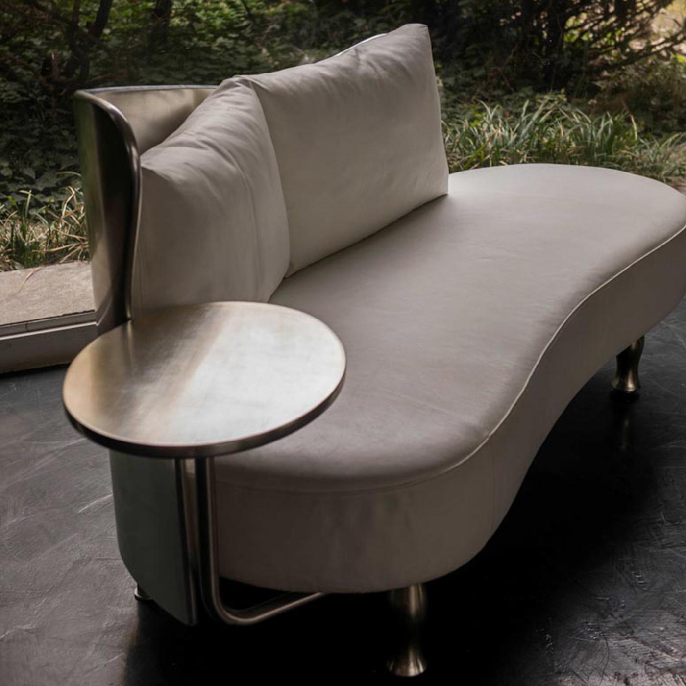A unique sofa, equipped with a swivel table attached that can be moved. The back is made of curved laminated wood and coated with silver leaf (option also available in gold leaf). The seat rests instead on a padded steel structure, is covered in