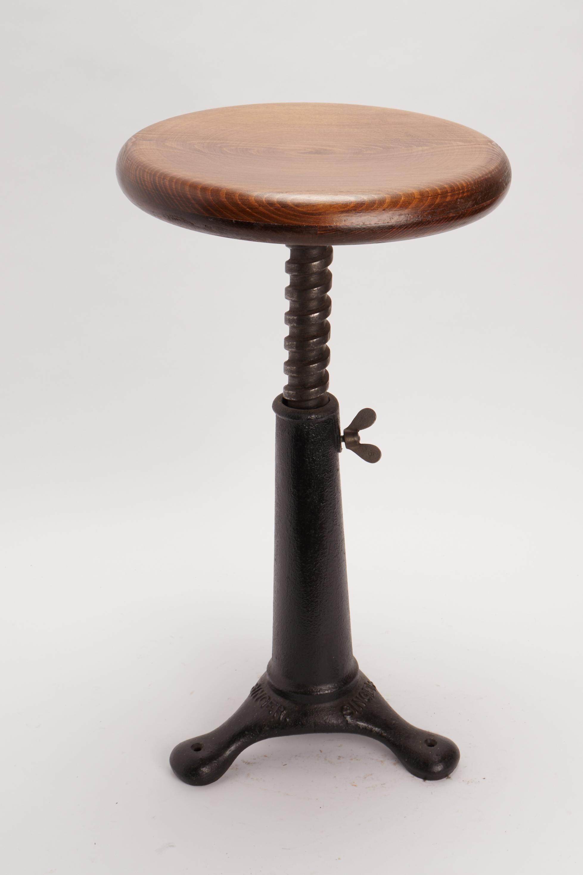 In 1910 Singer produced this adjustable stool for the textile industry. The leg is made out of cast iron and the sit is made out of solid Oak wood. Screwing or unscrewing the thick screw is possible to adjust the size of the stool. ( 31