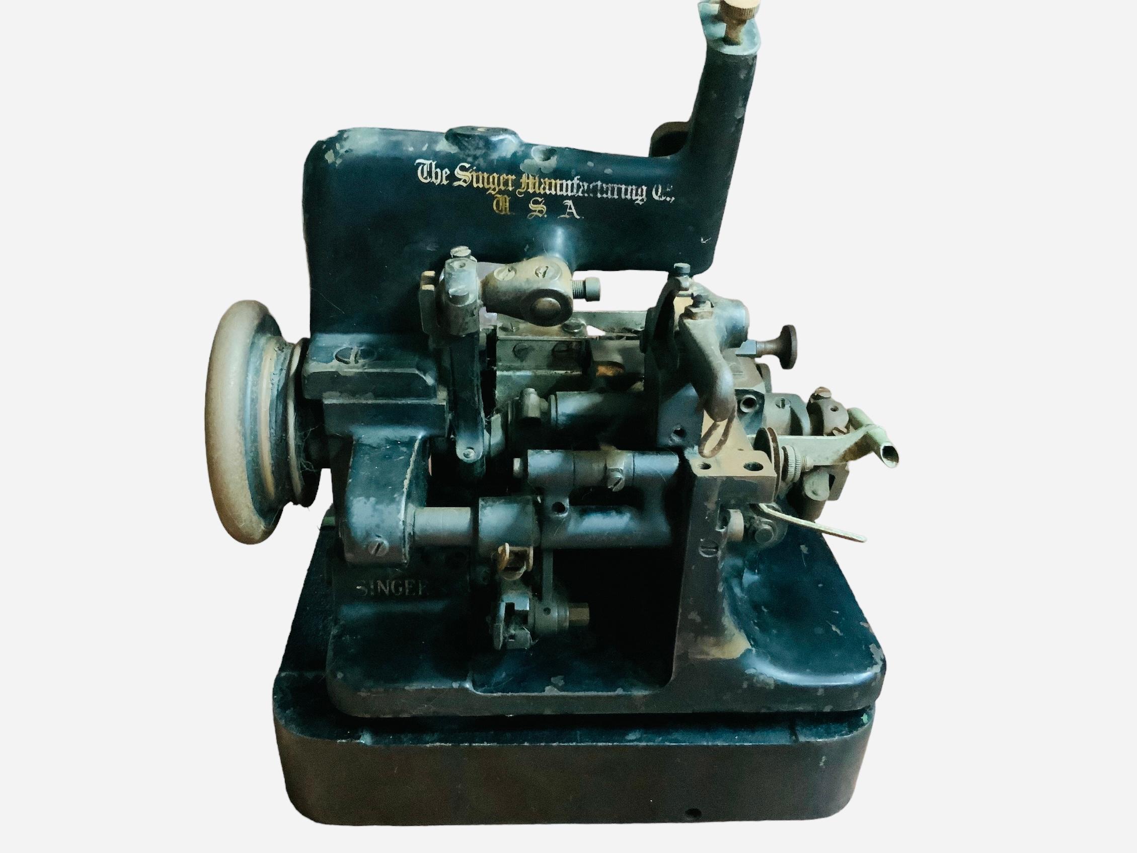 Dies ist eine Singer Manufacturing USA 81-5 Industrie-Nähmaschine. Es zeigt eine schwere, schwarz lackierte Nähmaschine aus Eisen, die mit goldenen Aufklebern auf der Vorder- und Rückseite verziert ist, die auf die Singer-Herstellung hinweisen. Die