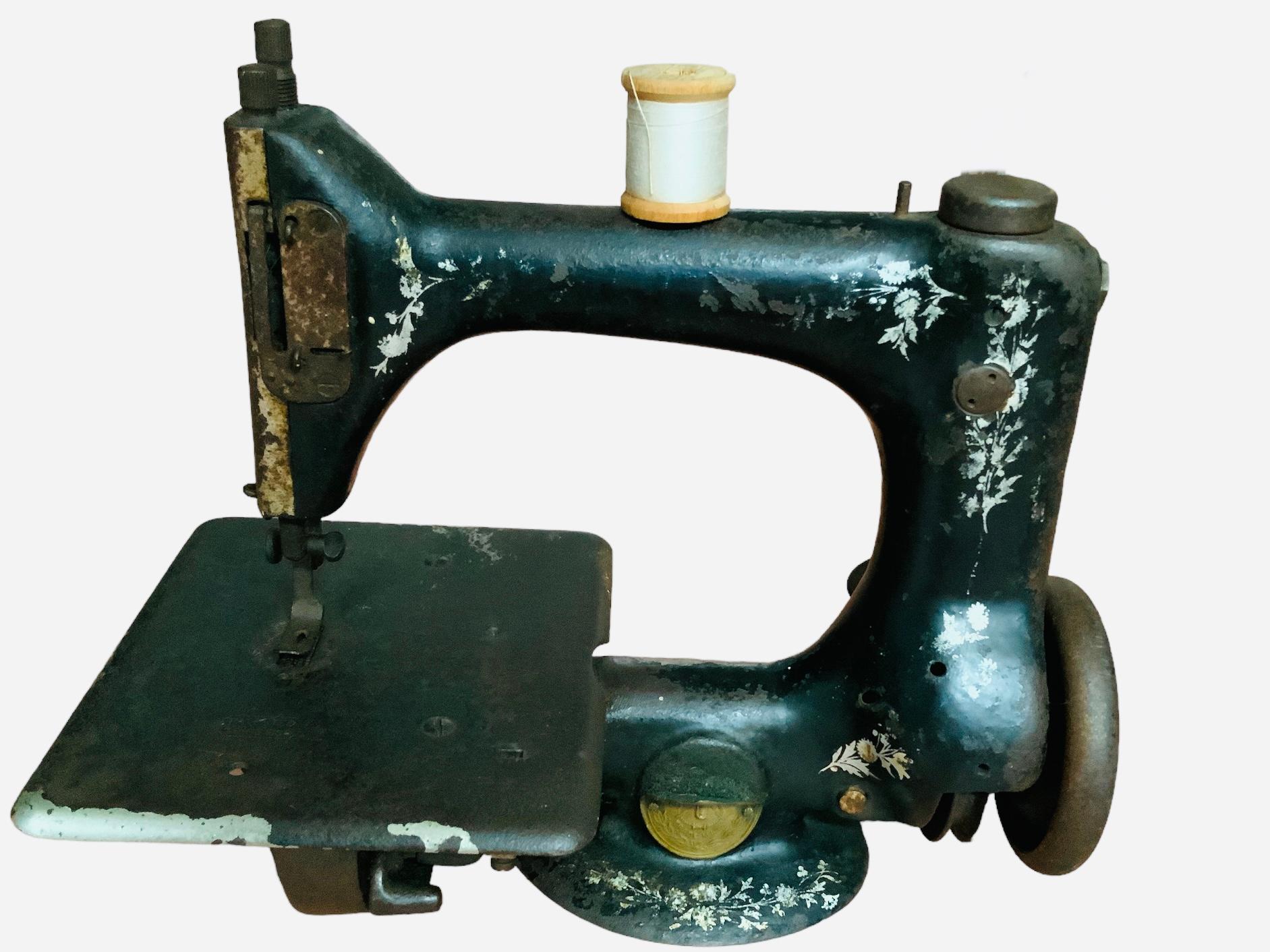 This is a rare Singer Model 24 chain stitch small sewing machine. Its background is painted black and adorned with red and white foliages decal. A gold color metal oval plaque identify it as the Singer Manufacturing Company trademark. This Singer