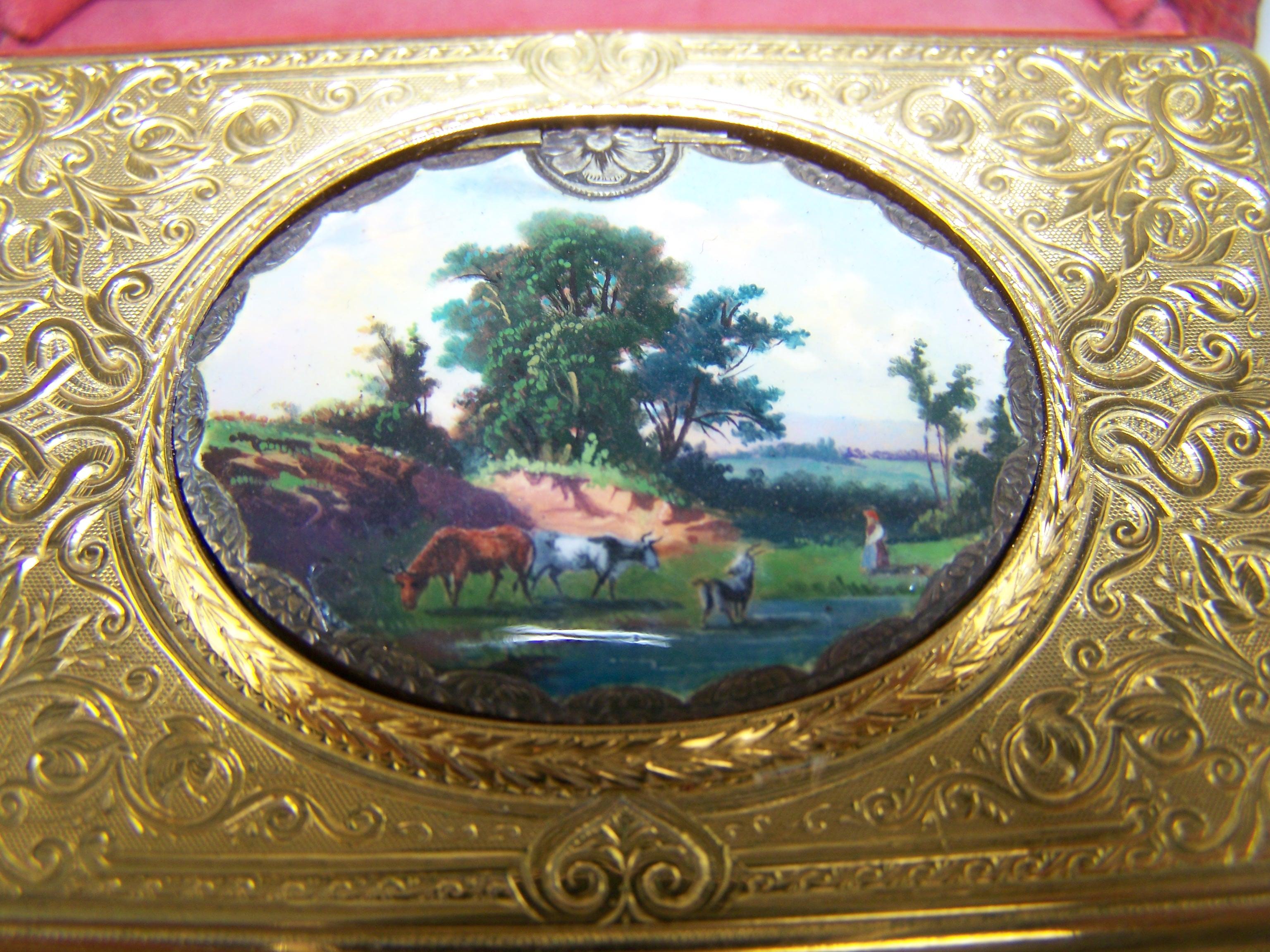 Rectangular silver guilded case with rounded corners. 
The oval lid has an enamel painting on the exterior of a mountain view and on the interior brightly enamelled with flower bouquets on a turquoise ground. When activated the lid opens to reveal 