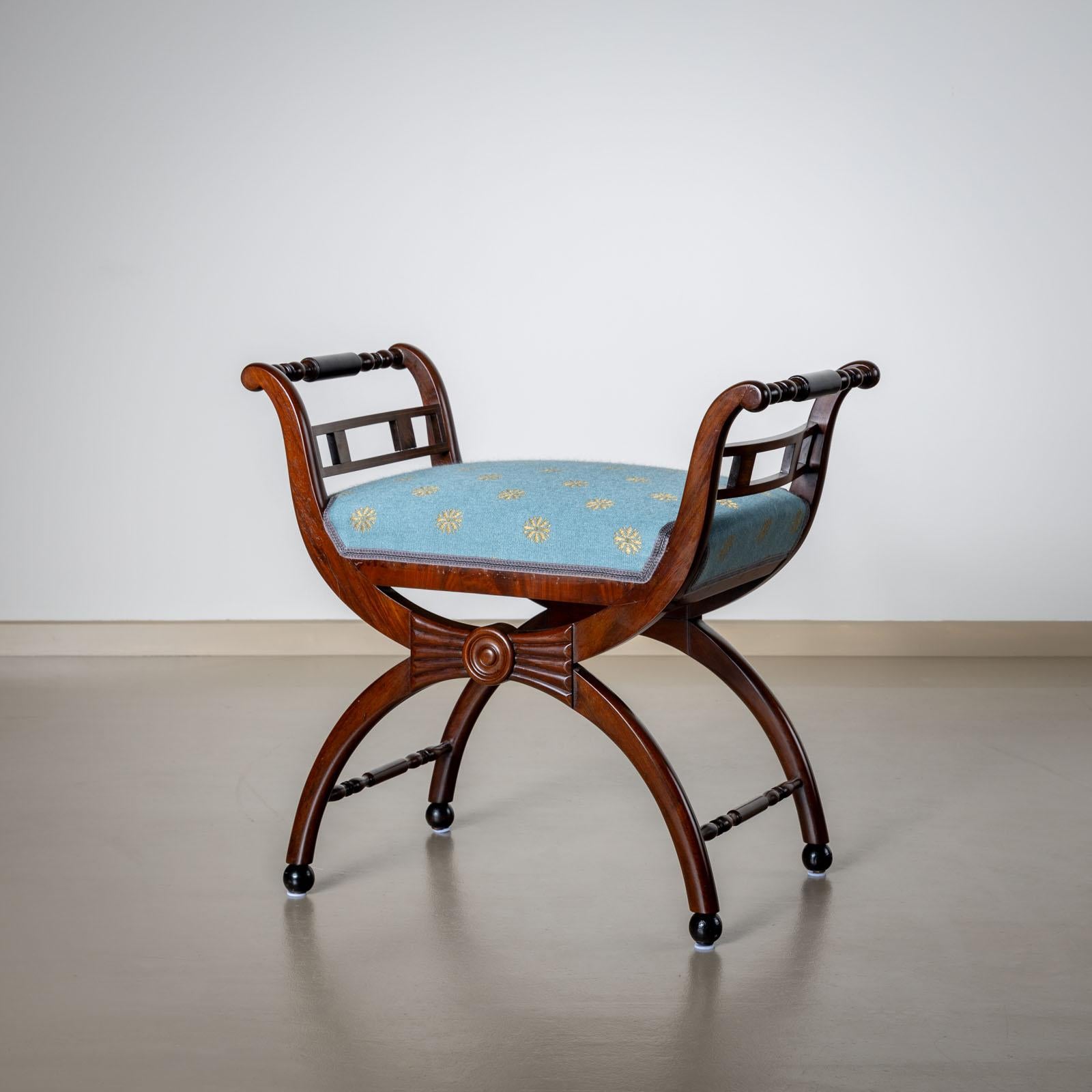Piccolo tabouret del XIX secolo su una struttura a x con braccioli torniti e piedi a sfera. 
Lo sgabello è rivestito in un tessuto azzurro con fiori dorati. 