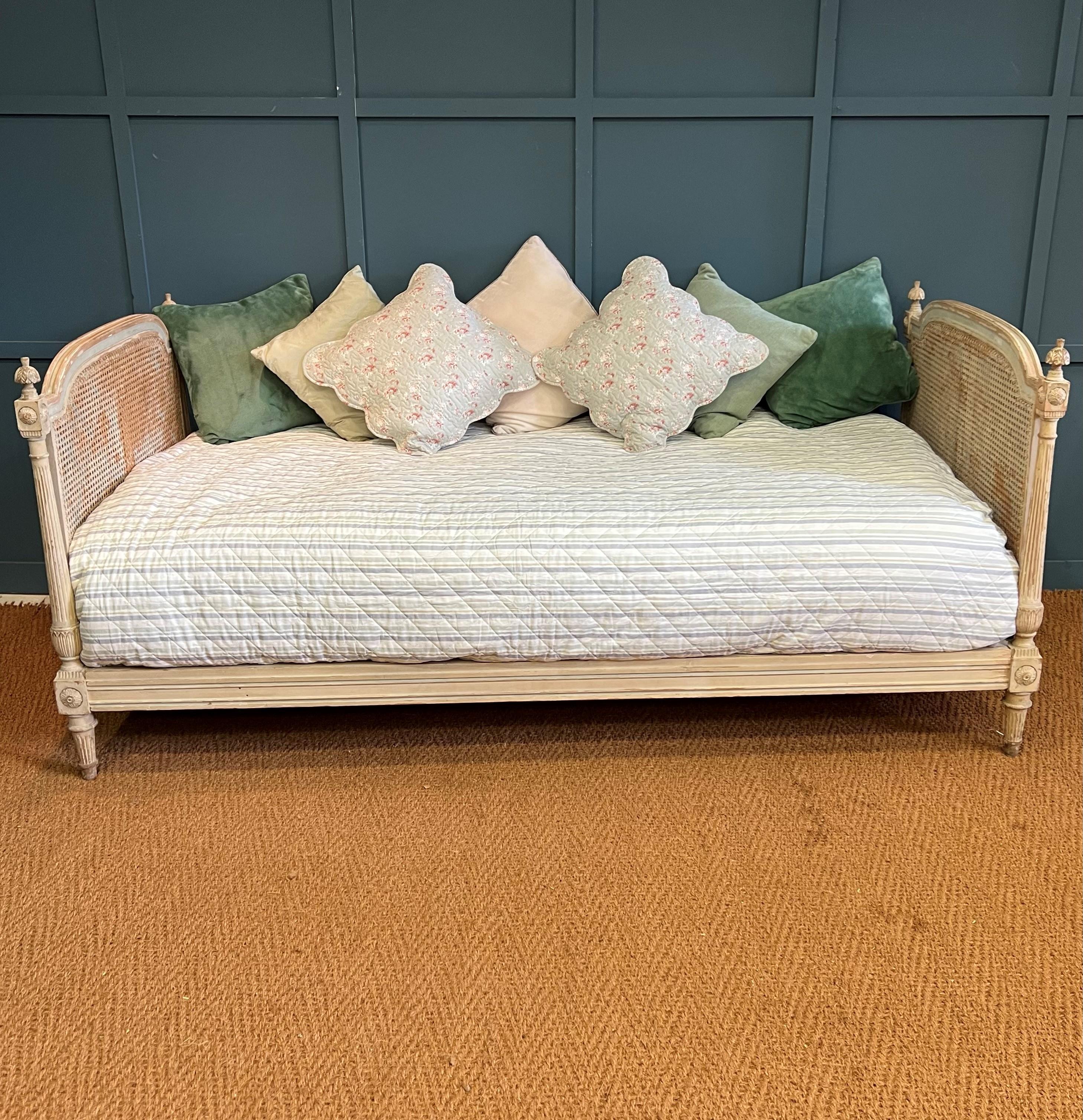 A very pretty antique French caned day bed. The frame has the original paint which has flaked off in places to expose the wood. On each corner is a cute carved palm tree. The day bed is made of a Beech frame and has very pale blue banding paint on