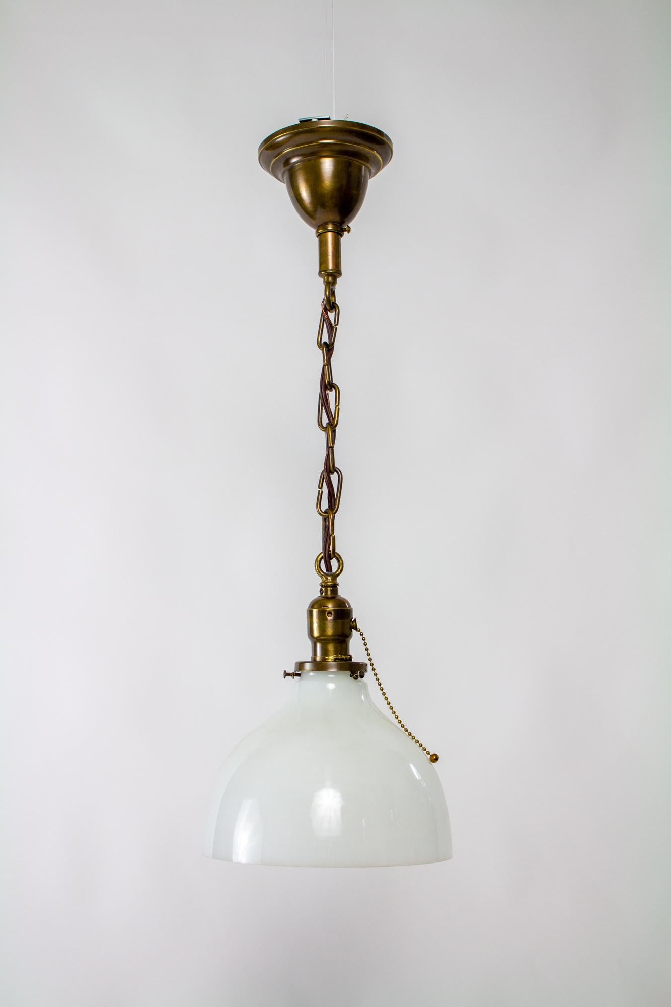 A classic hanging pendant light. White milk glass bell shaped shade. 2 ¼” fitter. Fixture and chain is brass with a medium patina. Single standard base bulb, 75 watt max. Completely restored and rewired, ready to hang. 24