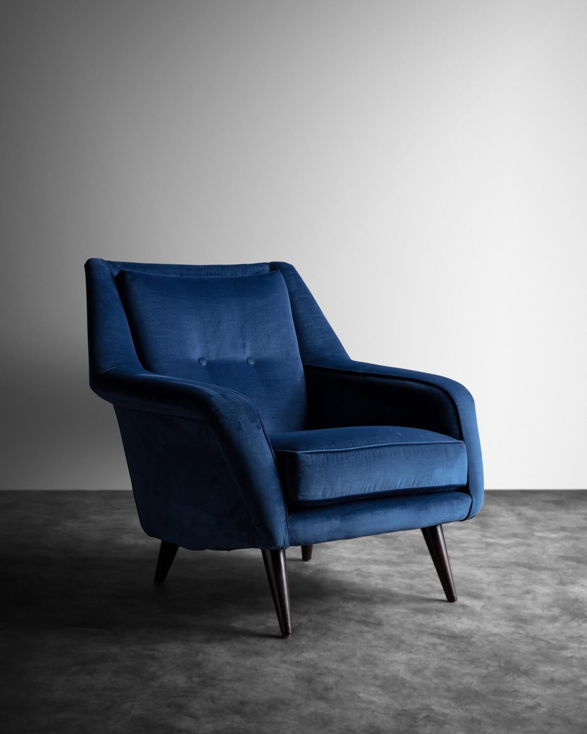 Over-upholstered chair with a steeply reclined back, down curved arms and four tapered tinted wooden legs.
       