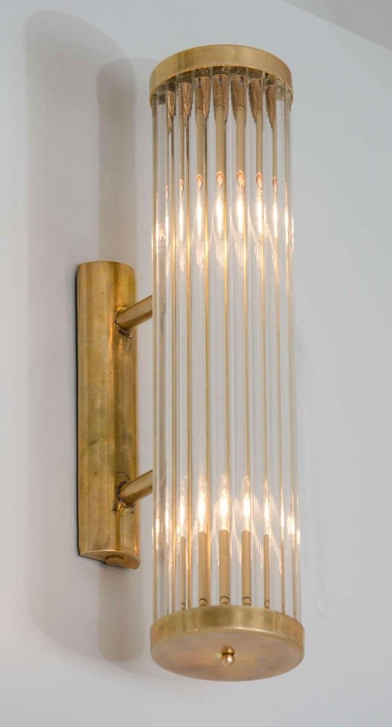 Contemporary Art Deco inspired Italian wall light in the style of ‘Venini’.
Each light comprises of a circle of slim Murano glass rods capped top and bottom by round brass plates that attach with two slim brass arms to a brass wall bracket.
Two