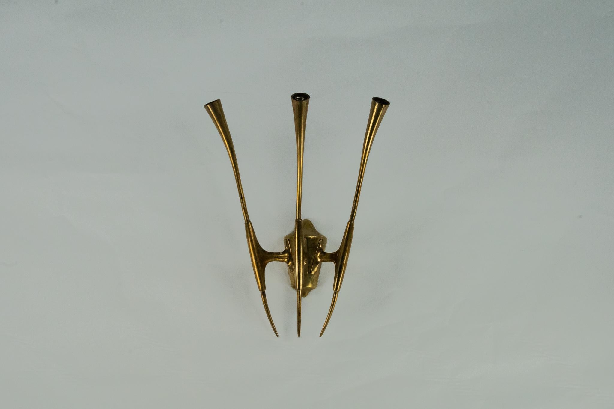 Brass wall sconce designed by Oscar Torlasco for Lumi Milano, crafted in the 1950s. This exquisite mid-century modern piece features three elegantly elongated and curved arms that extend gracefully from a sculptural central body. The sleek, organic