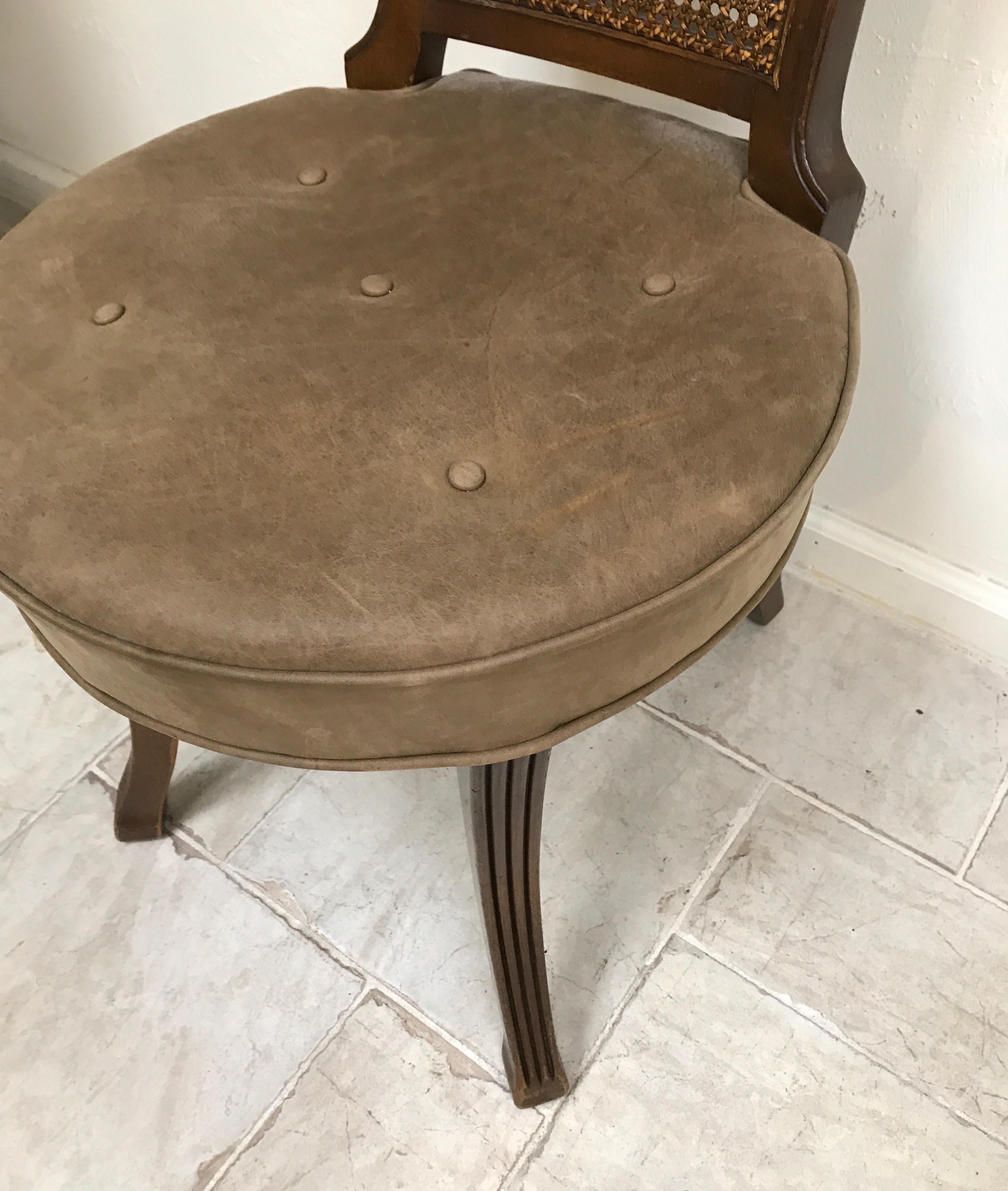 Single desk chair with round brown leather seat and cane back with brass handle on top.