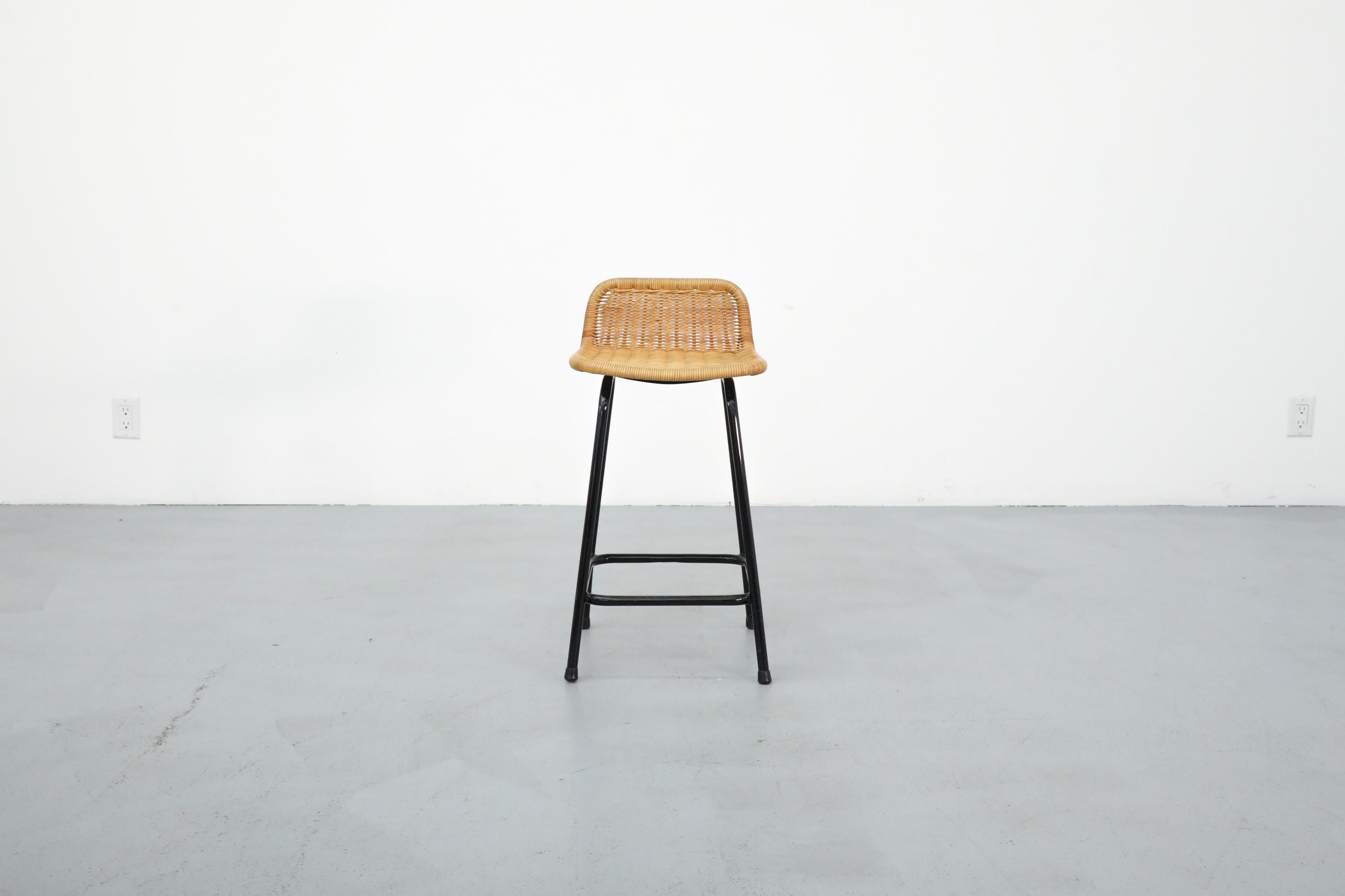 Single Charlotte Perriand style wicker Bar stool by Rohe Noordwolde. This stool has a woven seat and black tubular enameled legs. In original condition with visible wear consistent with age and use. Other similar stools available, listed separately.