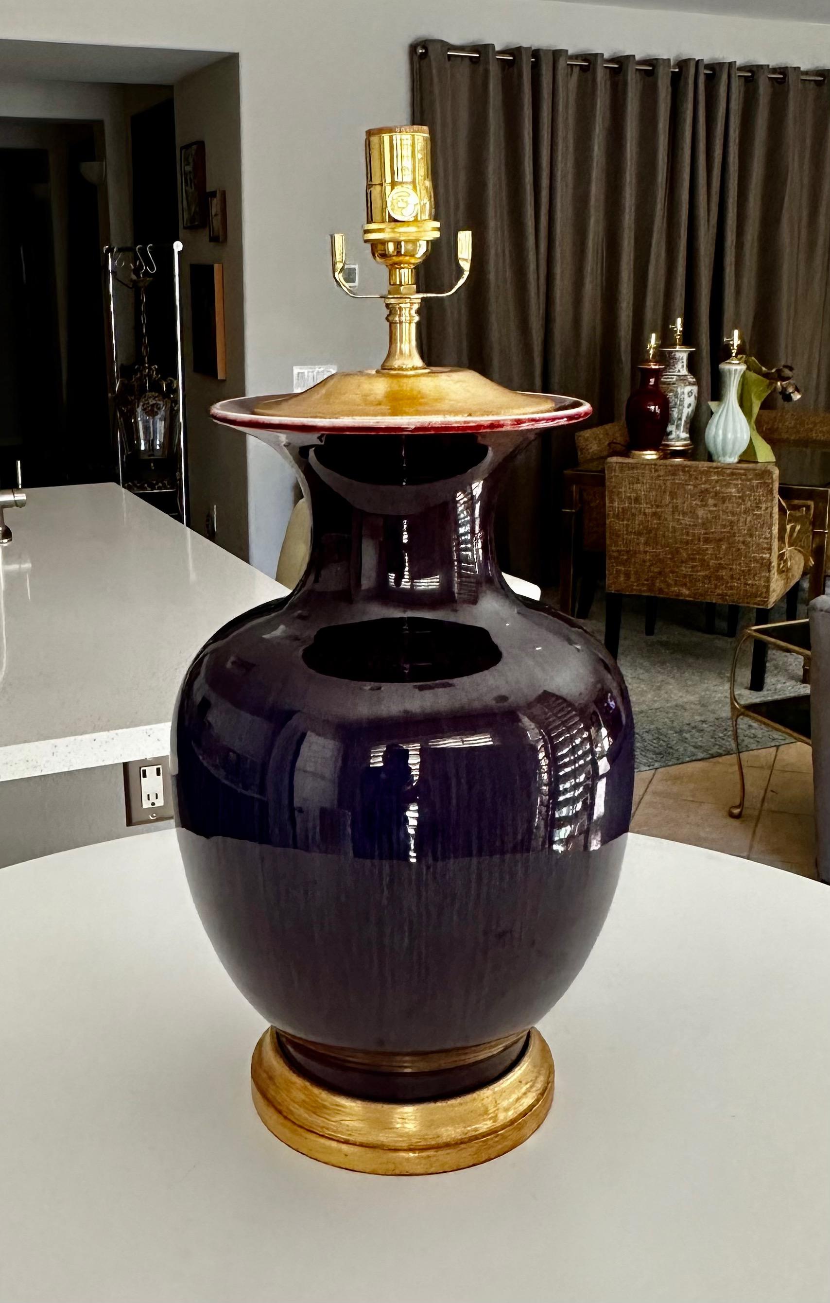 Single Chinese Asian Sang de Boeuf oxblood porcelain vase mounted on gilt turned wood lamp base. The coloring has an overall purplish tint with hints or red and vertical striping. Rewired with new 3 way brass socket and rayon covered cord.
Measures: