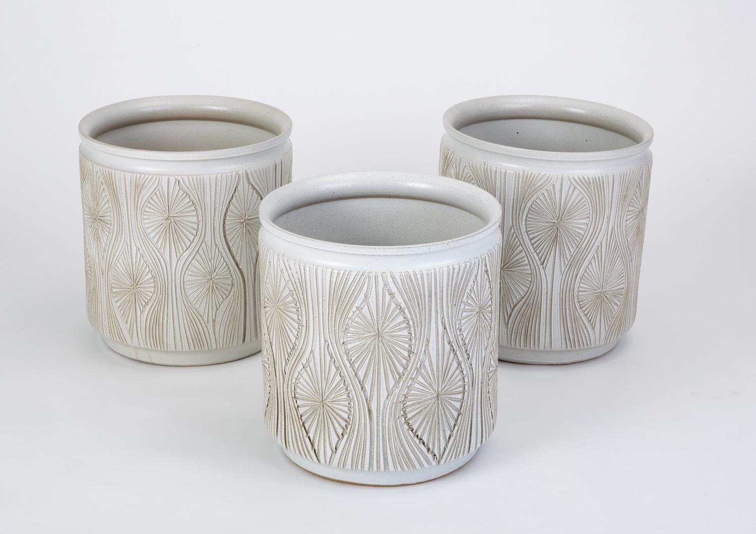 A tall, cylindrical planter from Robert Maxwell and David Cressey’s 1970s collaboration, Earthgender. This example has a slender lip, an allover incised pattern called ‘Teardrop Sunburst’ by the studio and is glazed white. We have three planters
