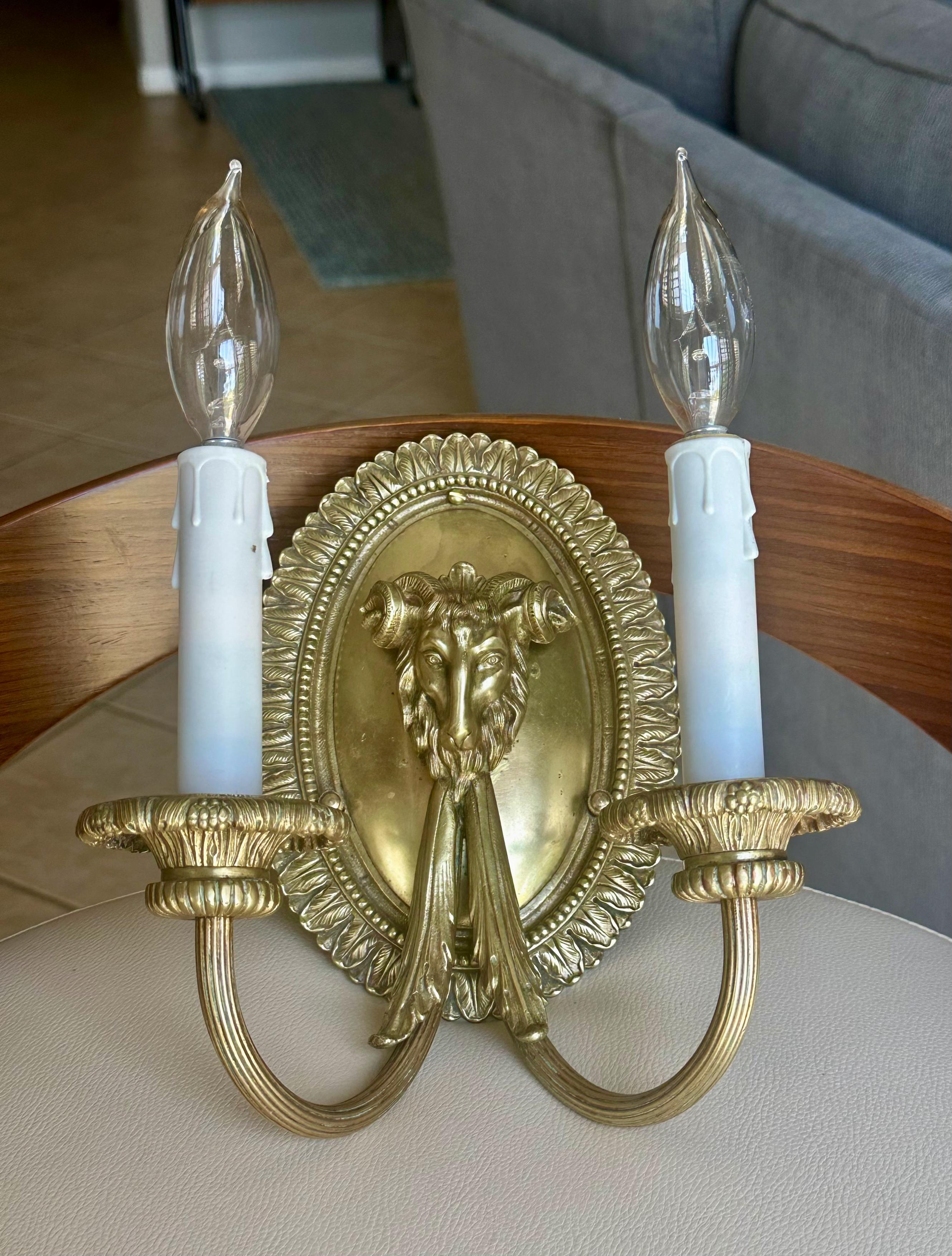 Apliques franceses de dos luces de estilo neoclásico decorados con motivos de cabezas de carnero. Fabricado por expertos con detalles de gran calidad. Utiliza 2 bombillas tamaño candelabro. 