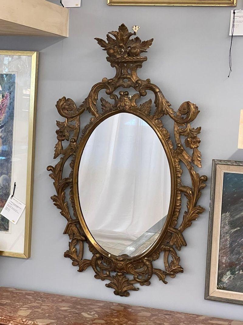 Single giltwood Italian floral motif mirror, wall / console / pier, Italy, 1960s.
 
A Italian wall or console mirrors. Each having pierced floral carvings terminating in a basket of flowers and fruit. The gilt gold frame flanking an oval shaped