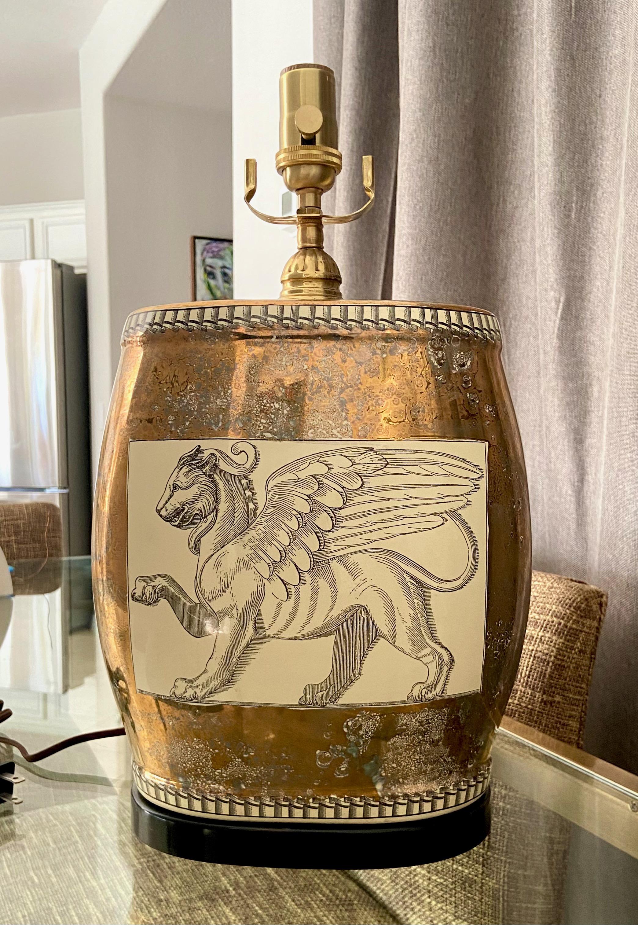 Single porcelain oval shape table lamp with Griffin Lion motif. The porcelain coloring consists black outlining of the Griffins against taupe background (front and back) surrounded by copper and black mottled mirror like finish. Lamp rest on black