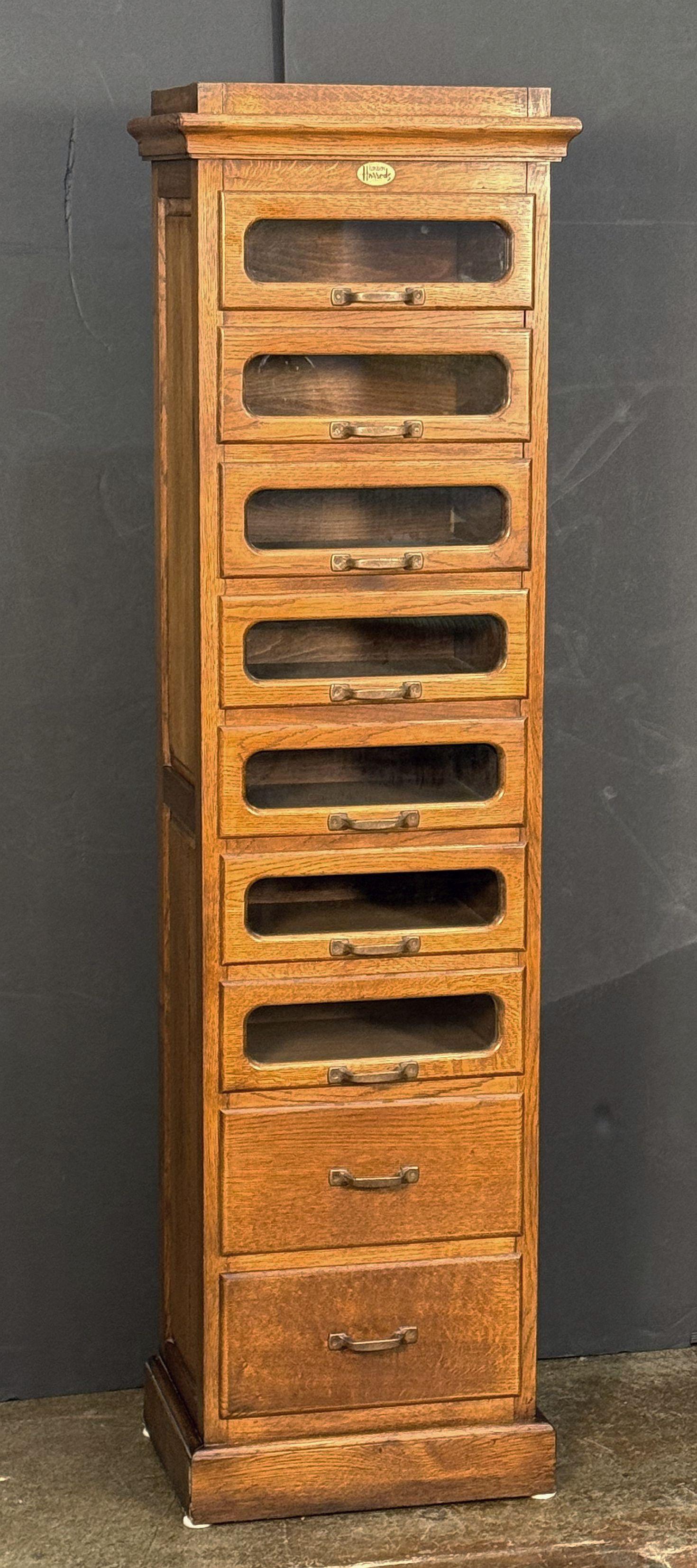 An exceptional vintage single haberdashery or haberdasher's cabinet of patinated oak, with paneled sides from Harrod's department store, in London, England featuring:

(7) glass-fronted drawers over two cupboard style drawers - (9) drawers