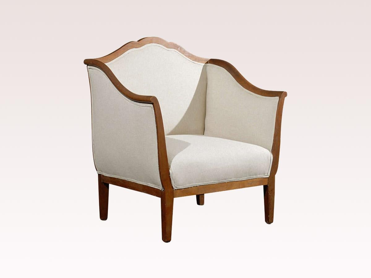 A single Italian upholstered club chair with walnut wood from the early 20th century. This antique chair from Italy is trimmed in an elegant walnut wood and has a gracefully arched top crest rail which flows down the shoulders, lining the top of