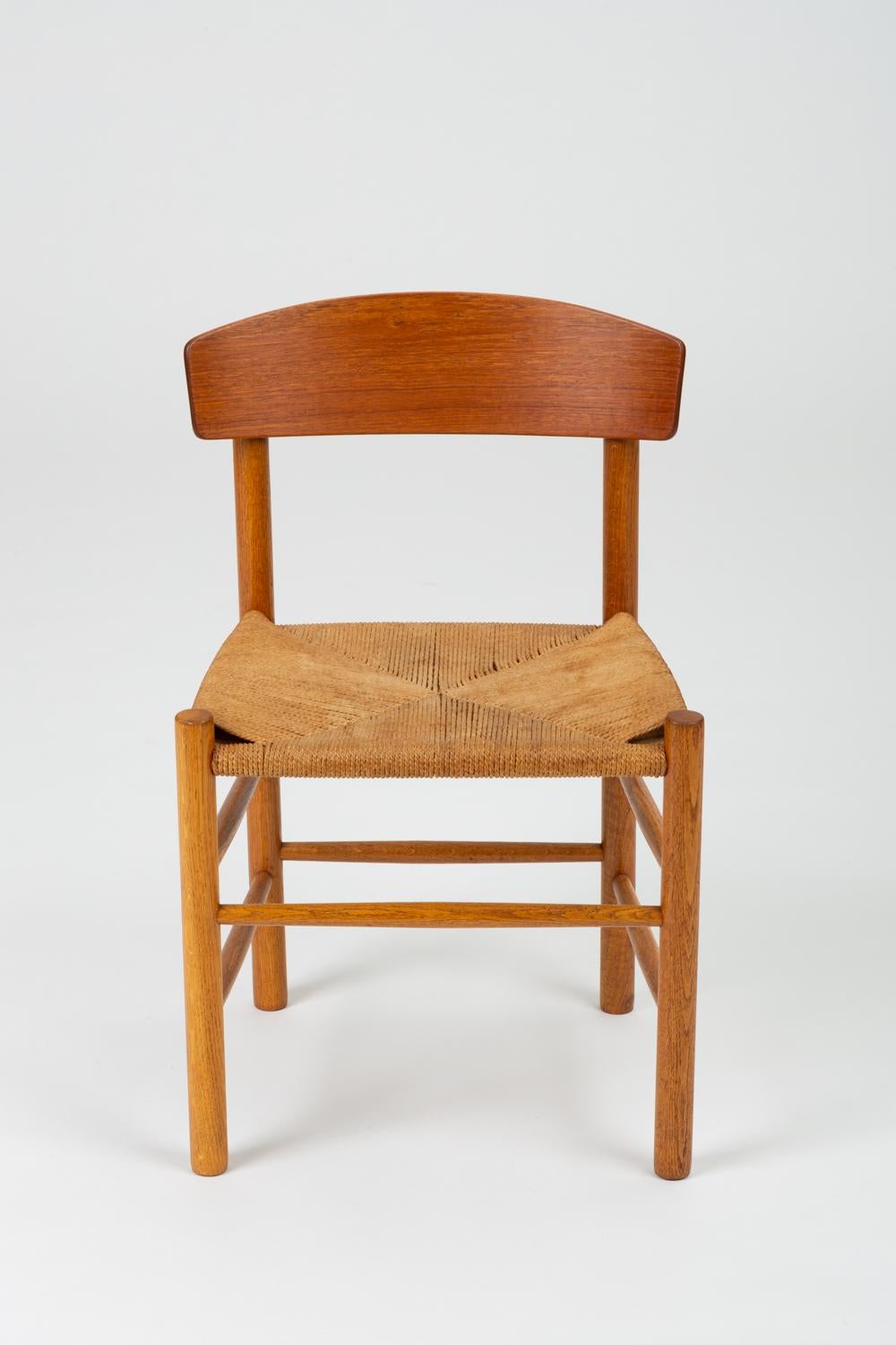 A single dining or accent chair by Børge Mogensen for FDB Møbler beginning in 1947. The J39 or “People’s Chair,” has a frame of oak dowels, with a wide, curved backrest and a woven seat in Danish paper cord. Contrasting wooden plugs cover the