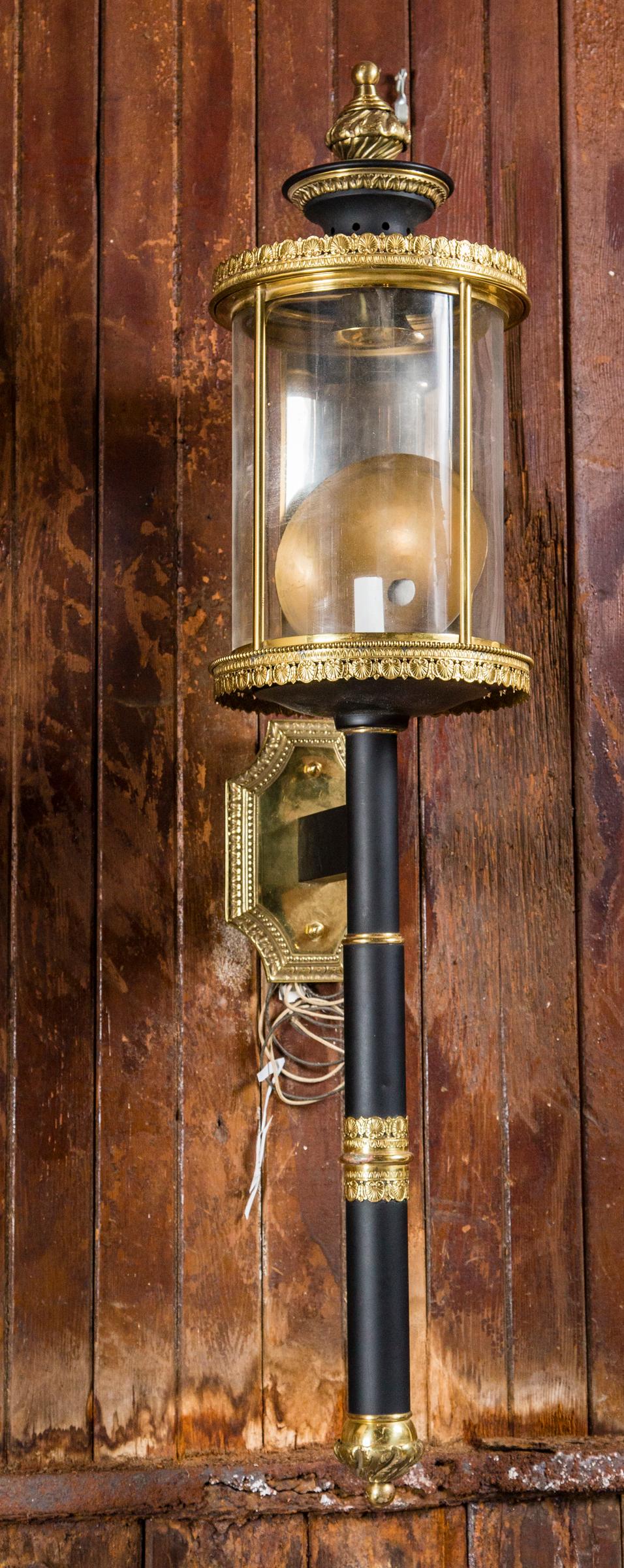 Old, new stock large single brass and black metal French sconce. Large cylindrical glass, heavy brass back plate. Back plate is 5.5 inches wide by 9.25 inches high.
