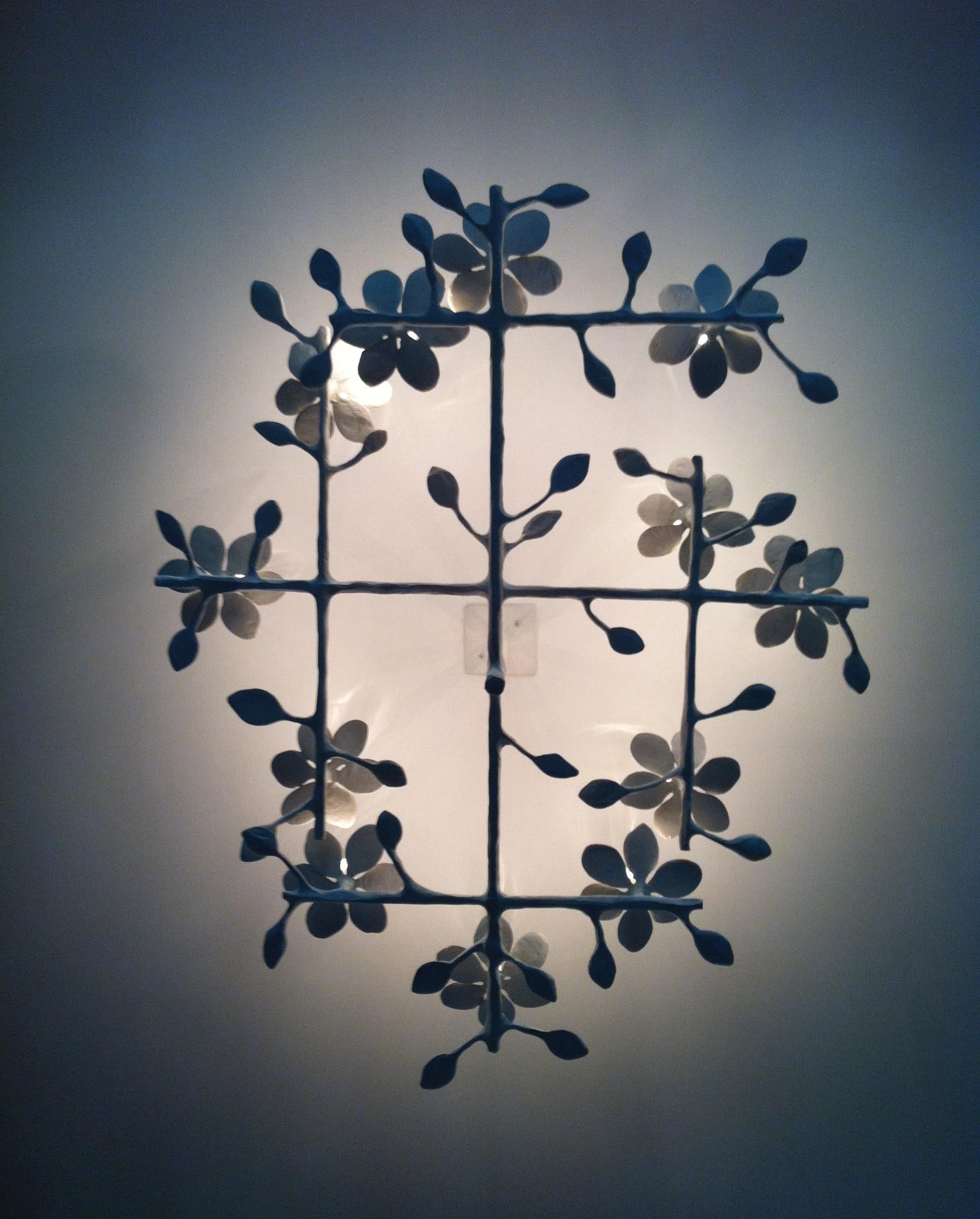 Single layer garden chandelier by Tracey Garet of Apsara Interior Design. The piece has 7 blooms each with a candelabra light and is shown in white plaster. The blooms are surround by branches and leaves. . The fabrication is plaster over steel
