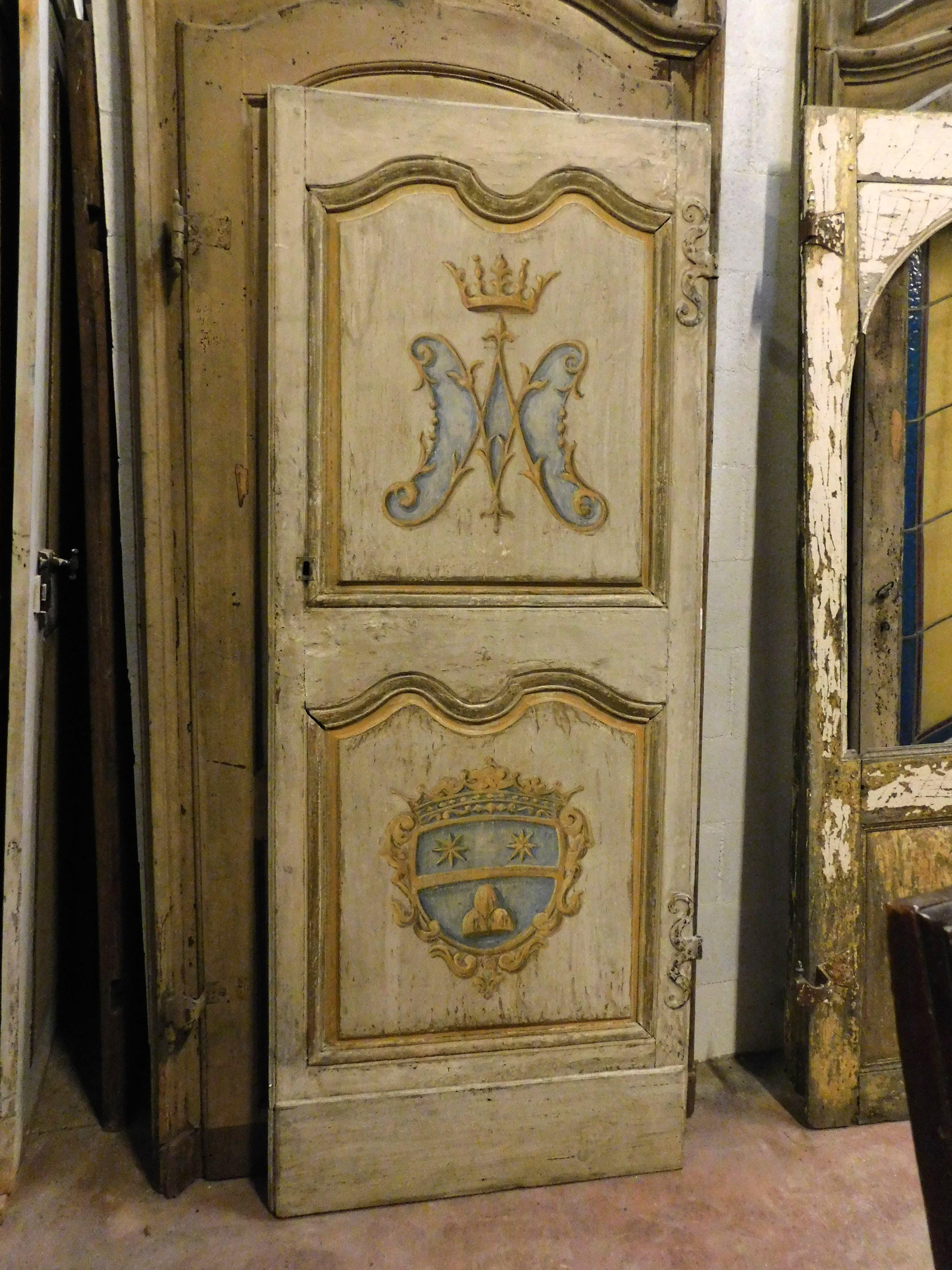 Puerta interior antigua de madera maciza lacada y pintada de una hoja, con paneles tallados y pintados a mano con dos escudos antiguos originales y típicos del siglo XVIII. Los escudos representan el símbolo mariano y debajo el escudo nobiliario de