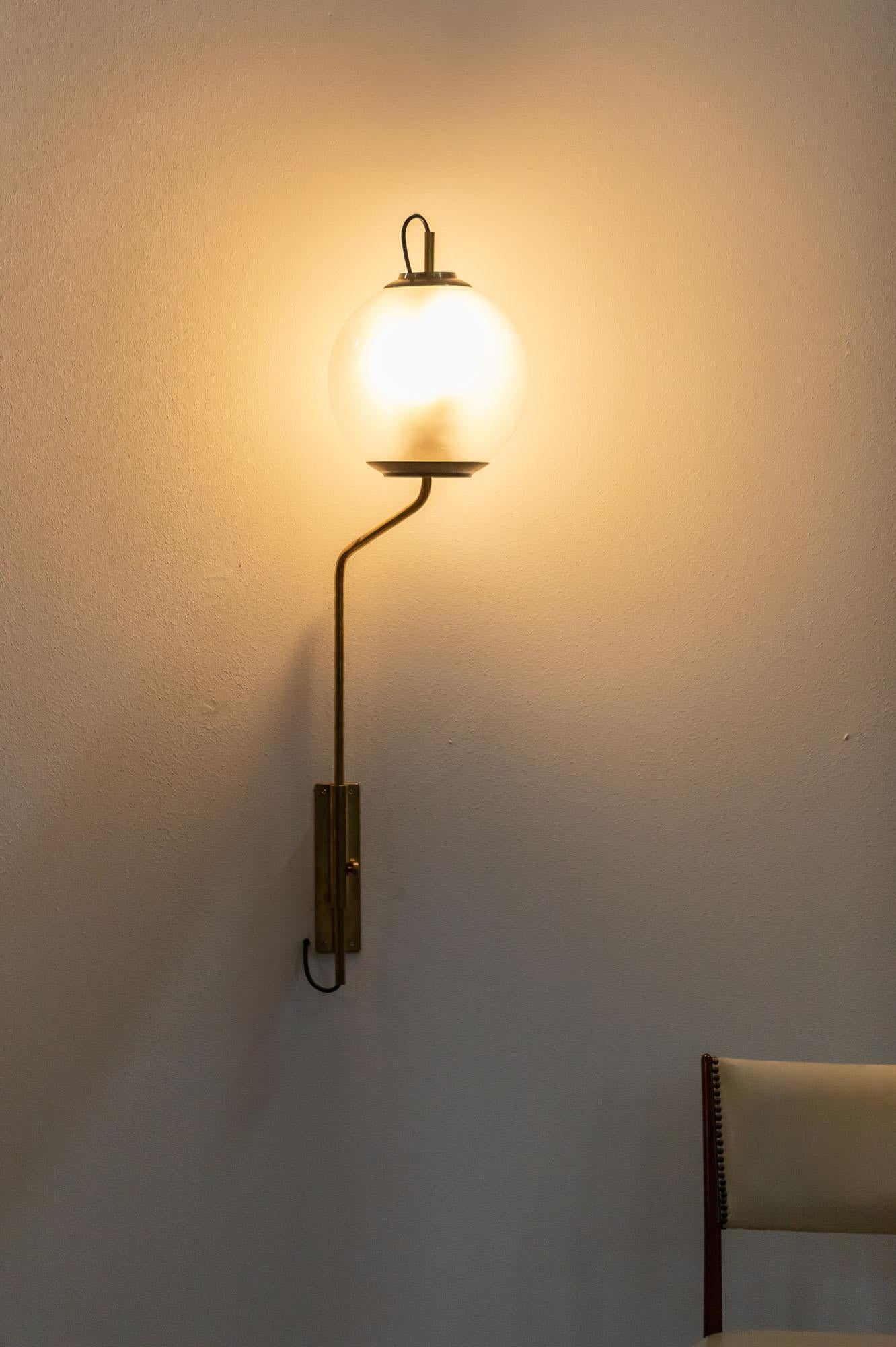 Iconic applique designed by Luigi Caccia Dominioni in brass, Model LP11. 
The lamp presents a thicker extremity of the structure with a brass plate to fix the applique on the wall. The glass light ball of relevant dimensions, is hold by a thin and