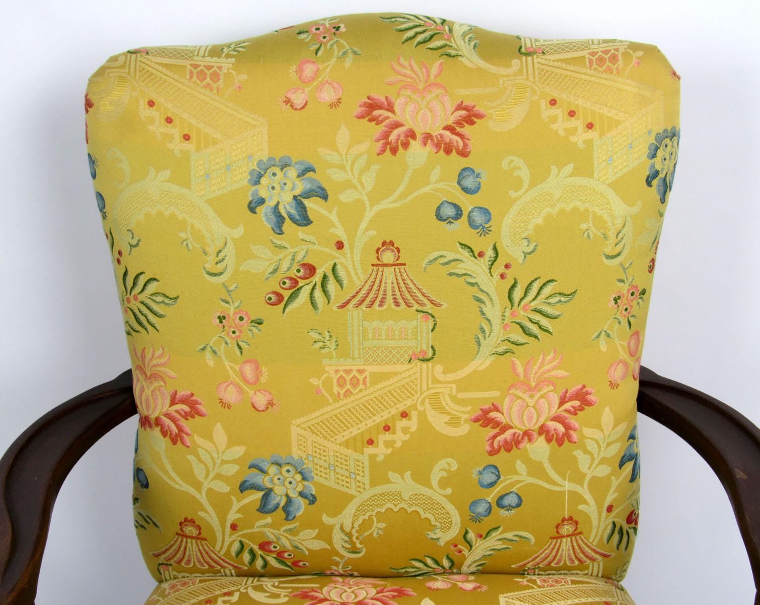 Single armchair with curved and scrolled mahogany arms and legs, upholstered in an oriental style fabric of yellow with pink, blue, and green floral detail.