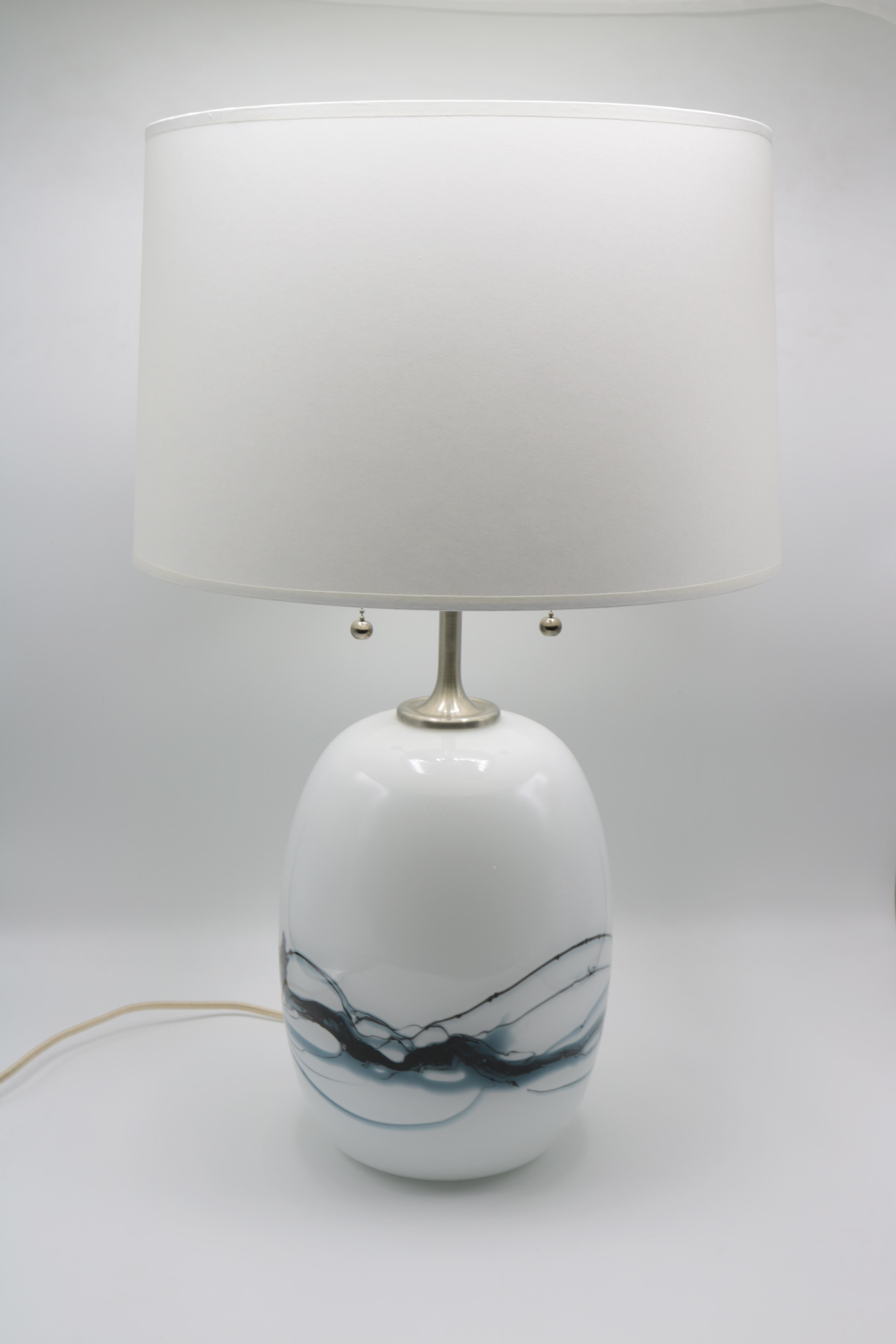 A modernist glass table lamp designed by Michael Bang for Holmegaard.
White glass with blue colored swirl patterns and brushed nickel neck.